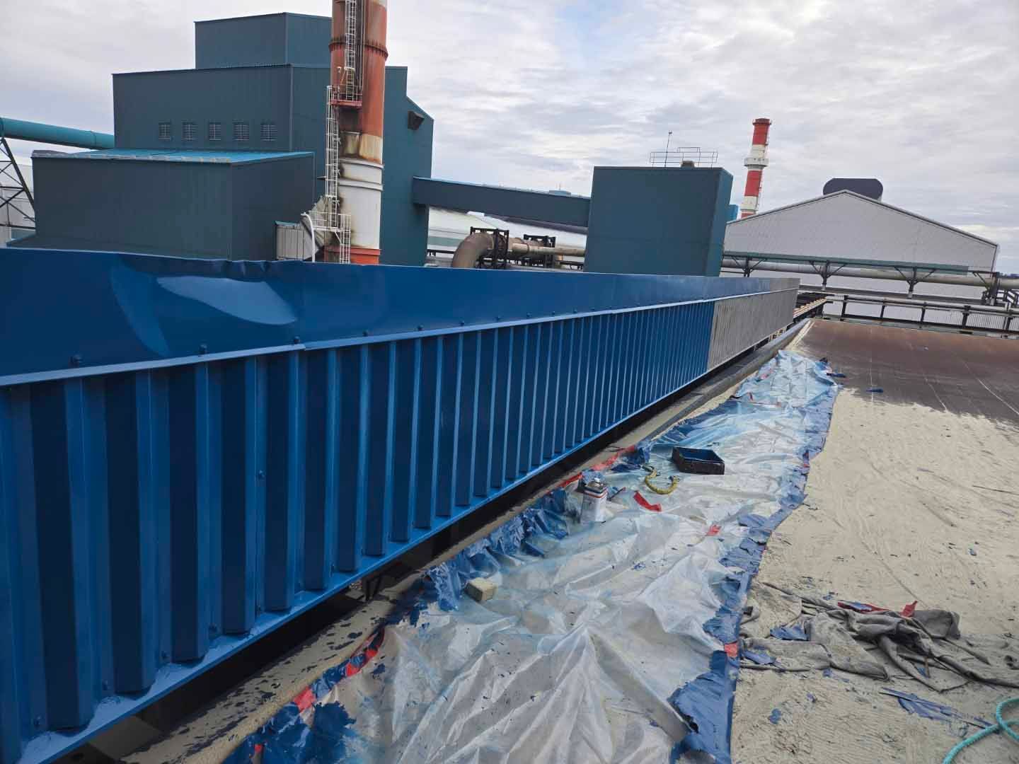 Une structure industrielle bleue est en cours de peinture, sur fond industriel avec une bâche bleue.