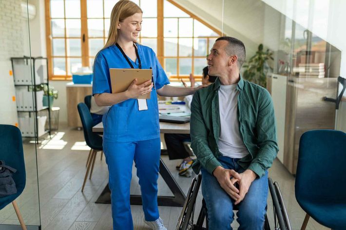 A nurse is talking to a man in a wheelchair in a waiting room.