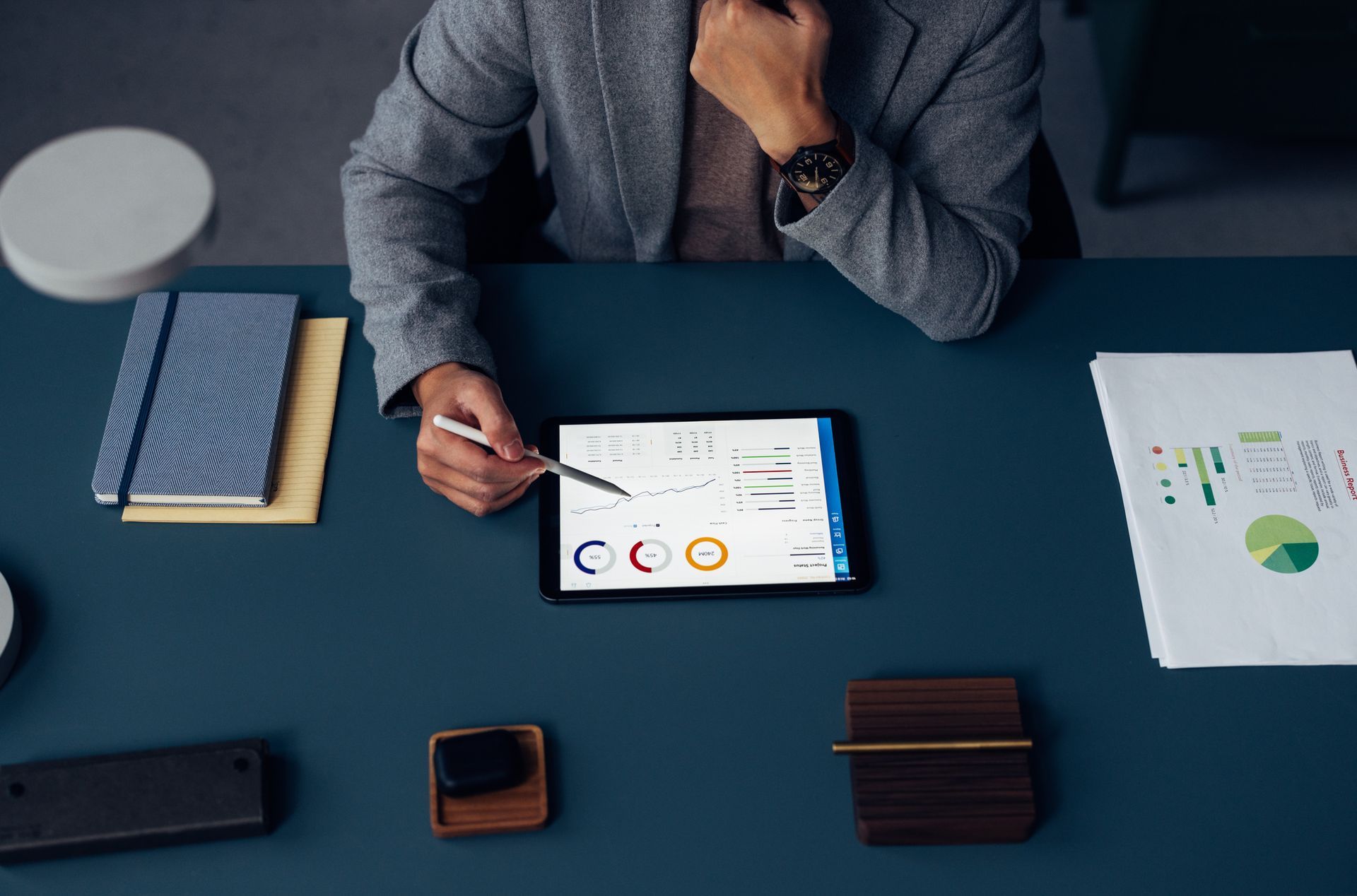 Professional analyzing financial reports with tablet at office desk.