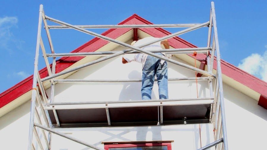 A man is standing on a scaffolding on top of a house.