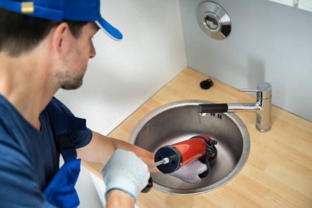 A man is using a plunger to unblock a sink.