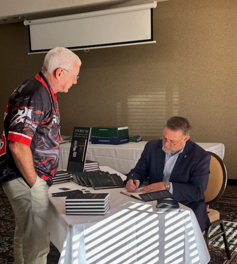 A man standing next to a man sitting at a table