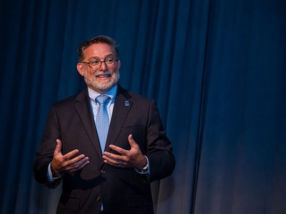 A man in a suit and tie is standing in front of a blue curtain.