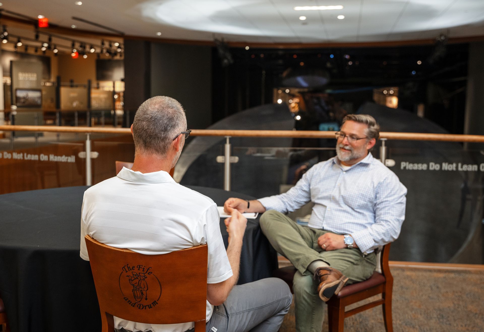 Two men are sitting at a table talking to each other.