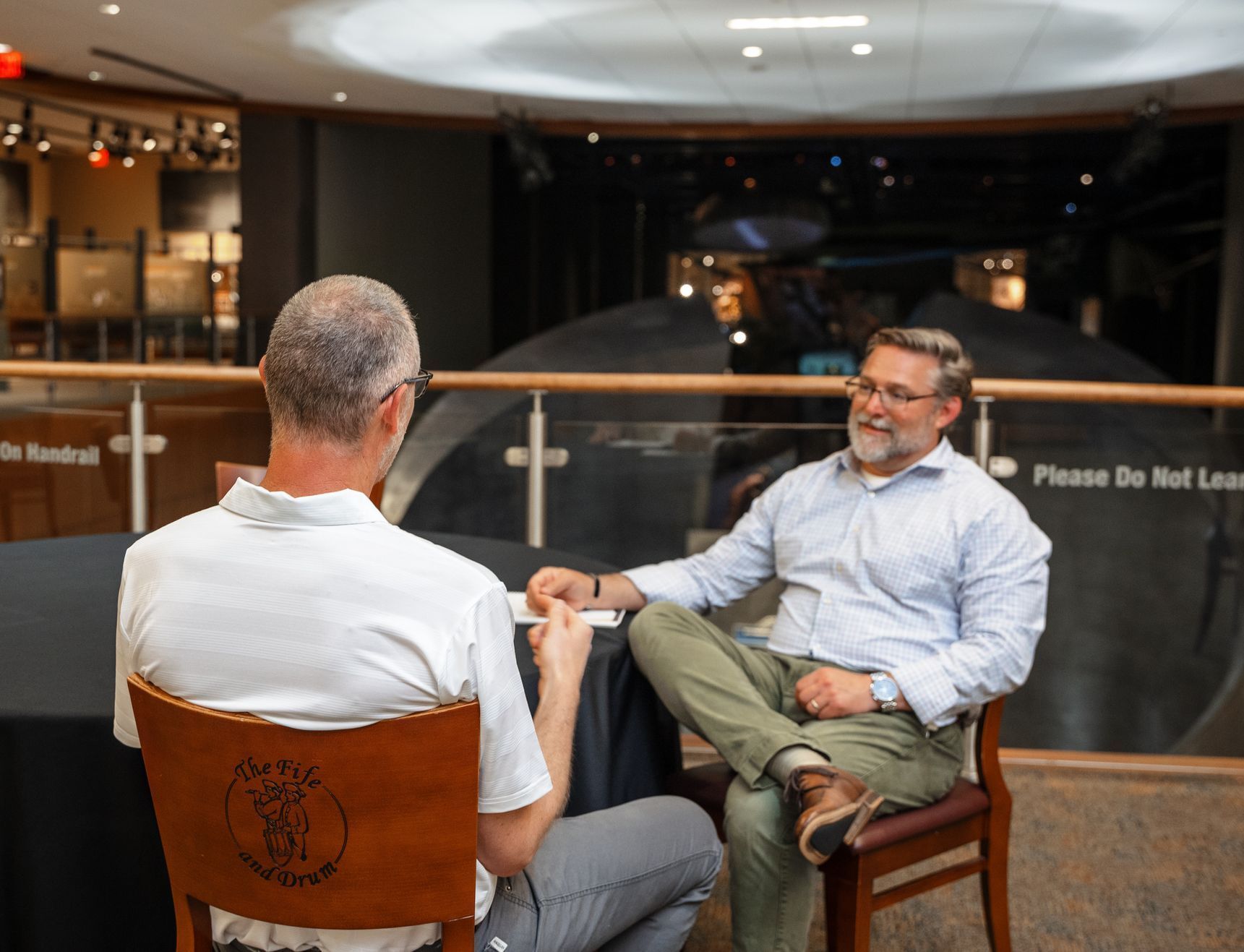 Two men are sitting in chairs talking to each other.