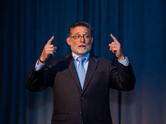 A man in a suit and tie is giving a speech on a stage.