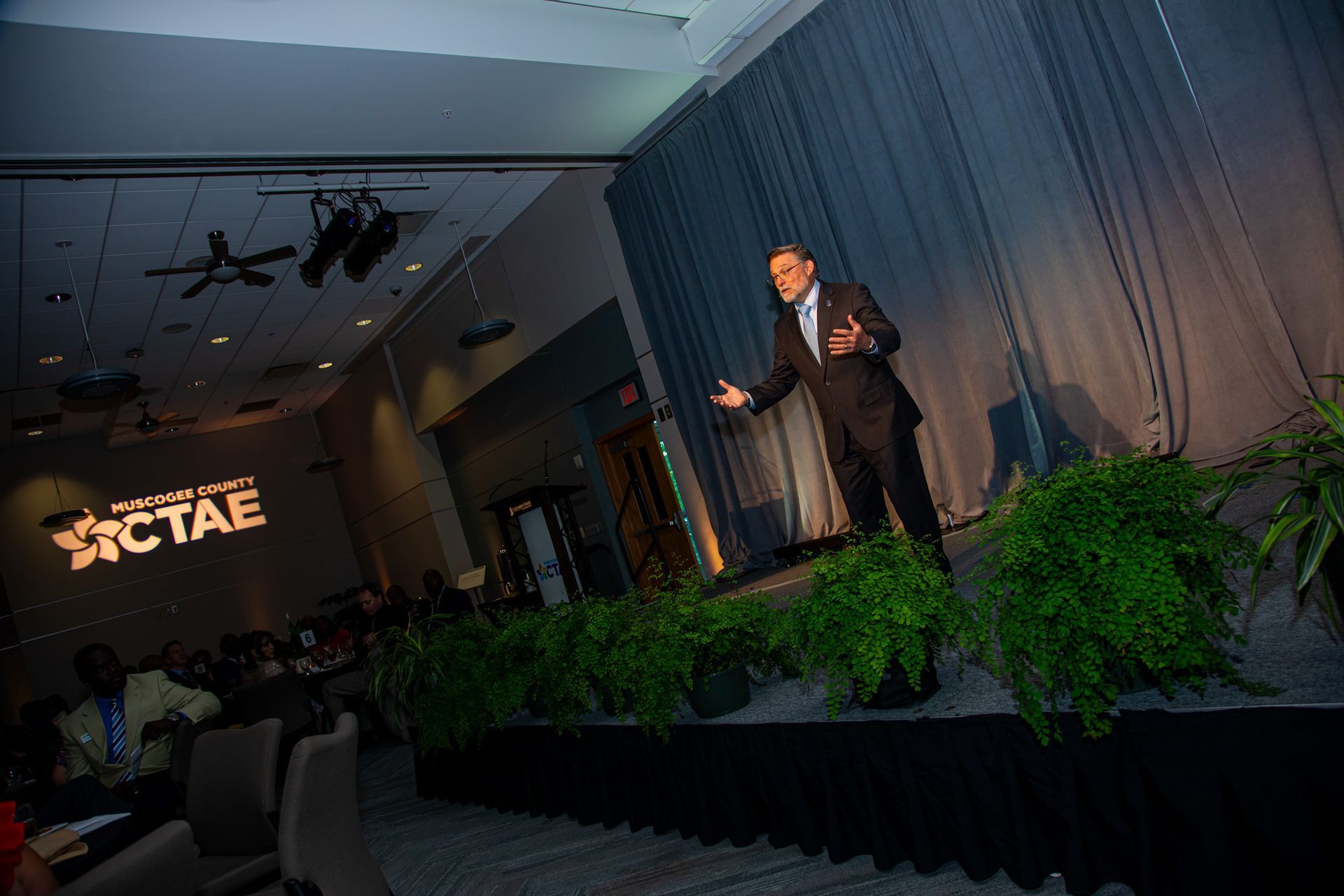 A man in a suit is standing on a stage giving a speech.