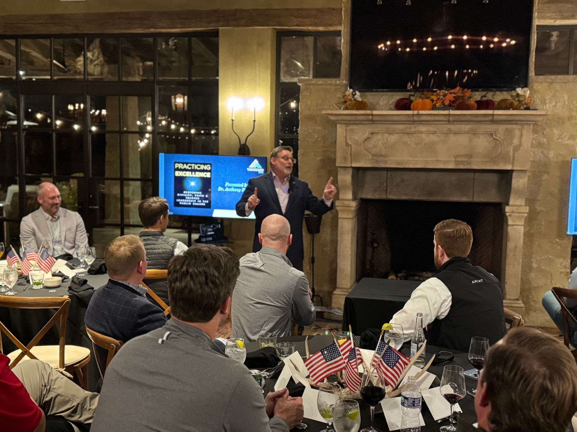 A man is giving a presentation to a group of people sitting at tables.