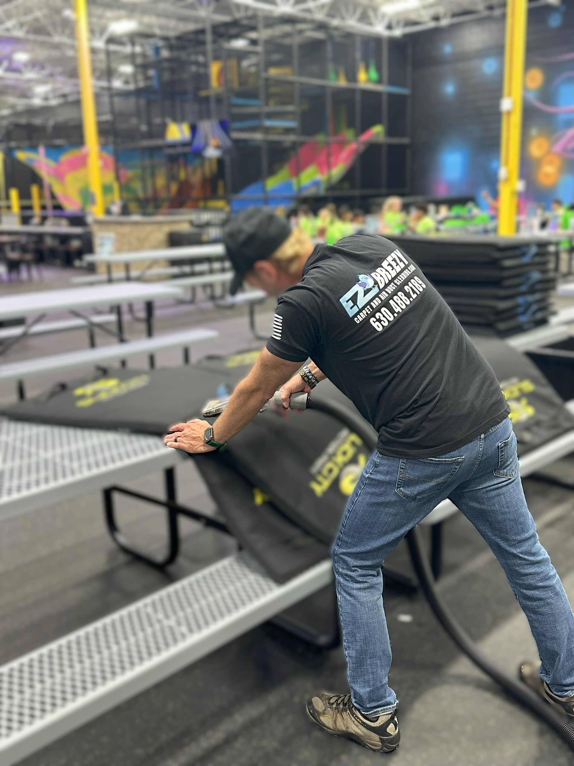 Man arranging black mats at an indoor trampoline park.