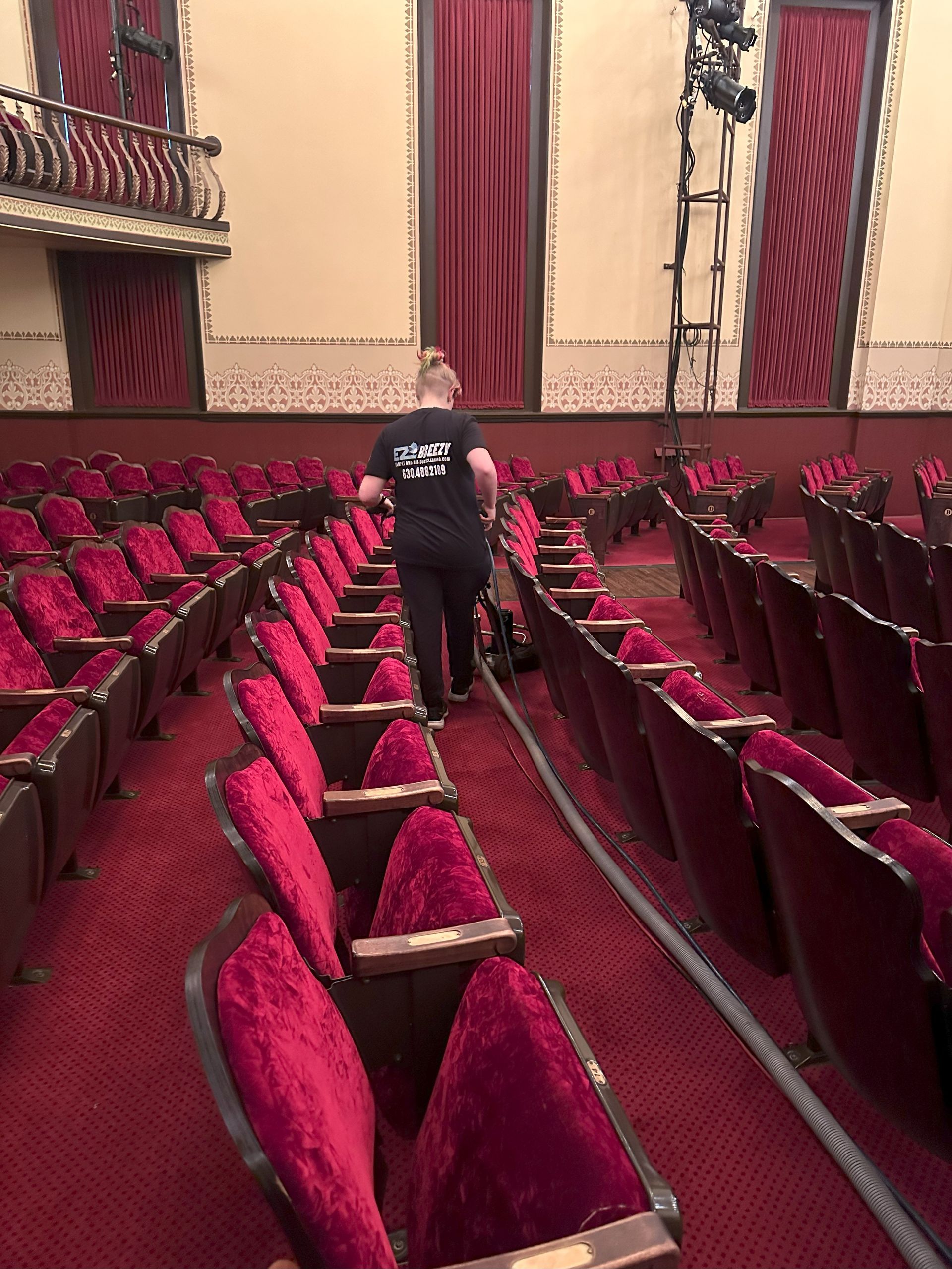 Person walking through rows of red velvet theater seats toward the stage.