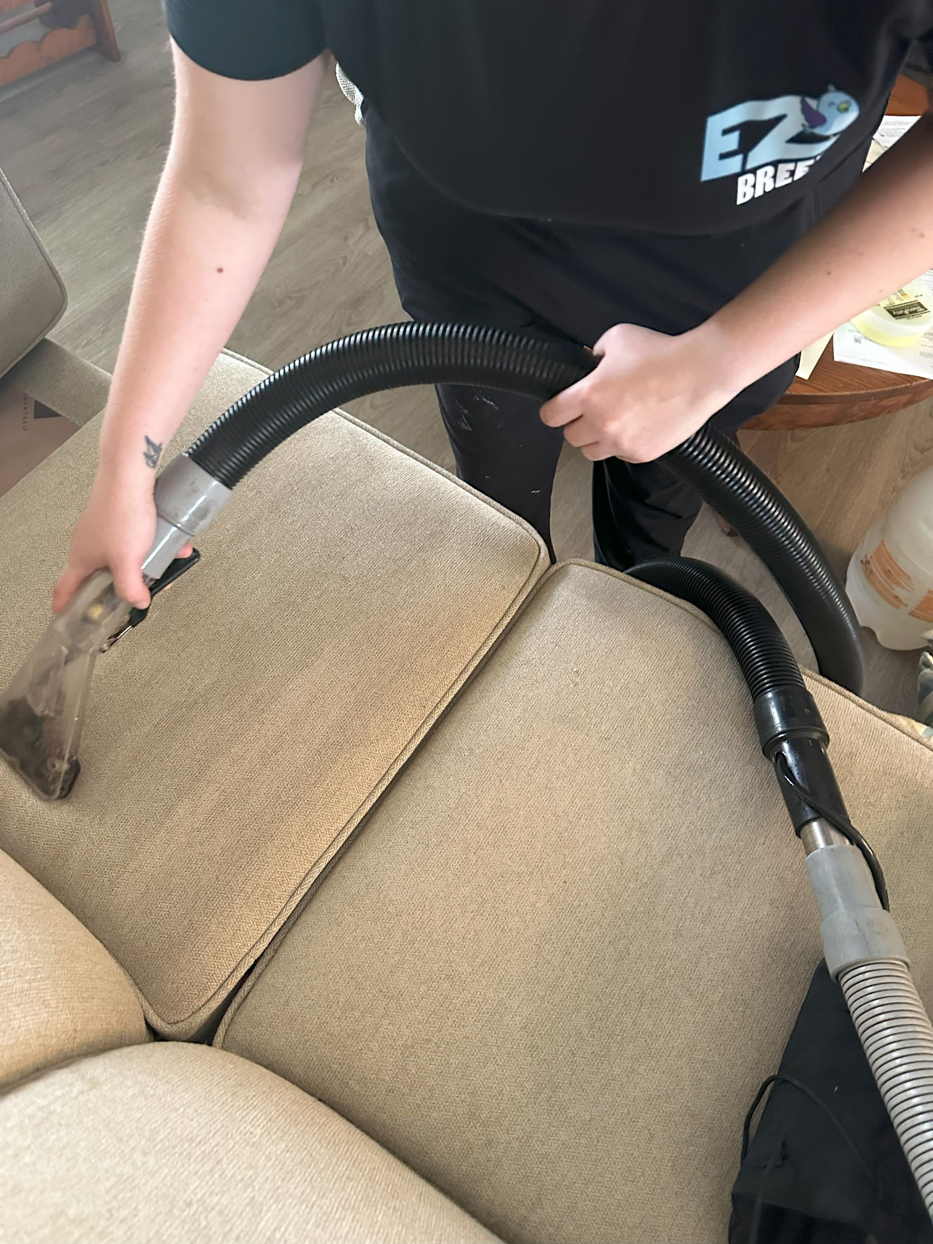 Person cleaning a beige couch with a vacuum hose attachment.