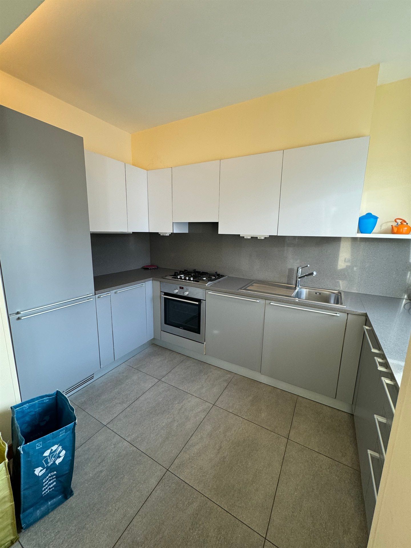 A kitchen with white cabinets , a stove , a sink , and a trash can.