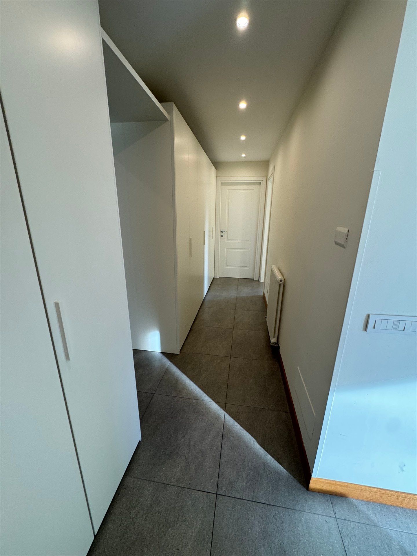 A long hallway with white cabinets and a door