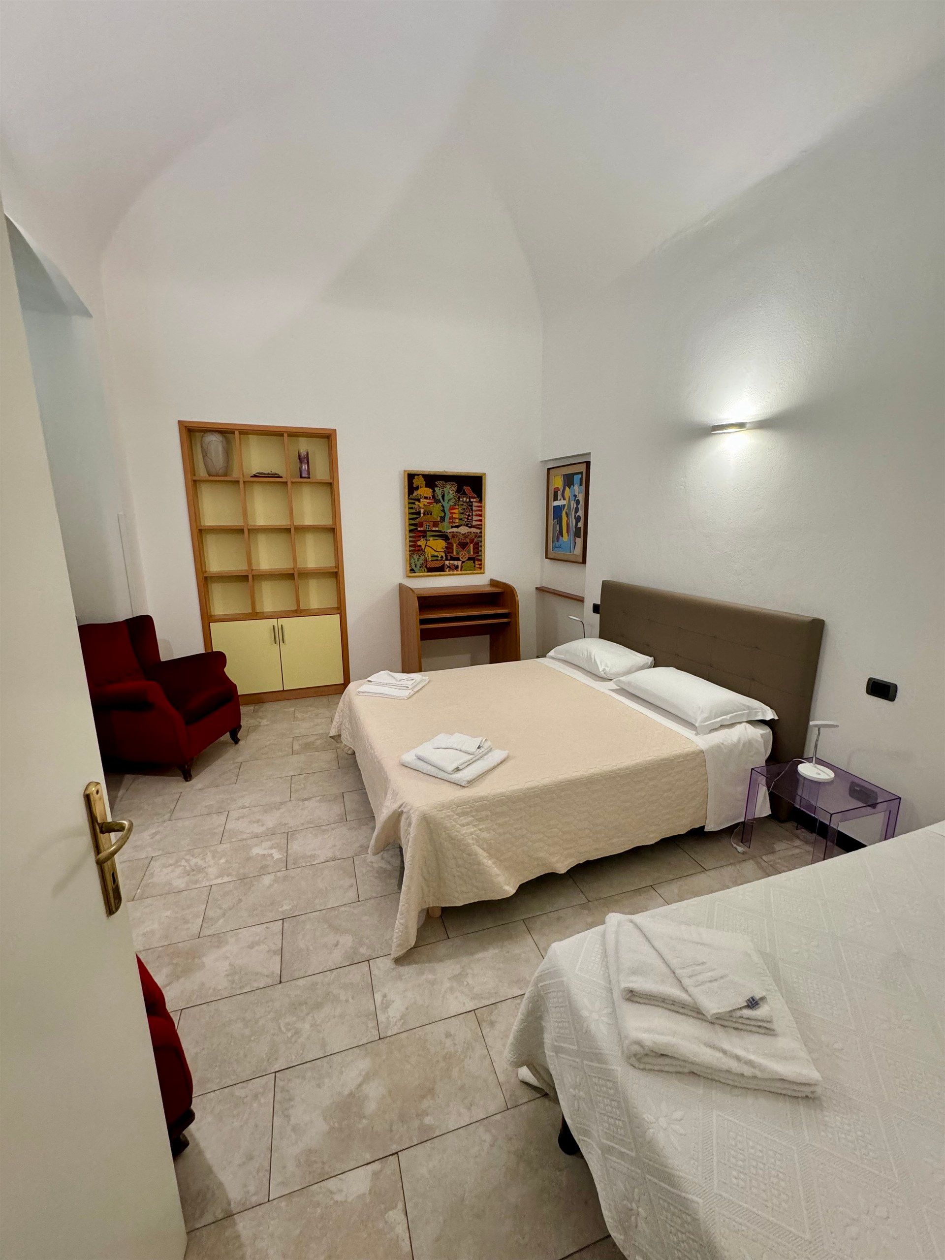 A bedroom with two beds , a chair and a bookshelf.