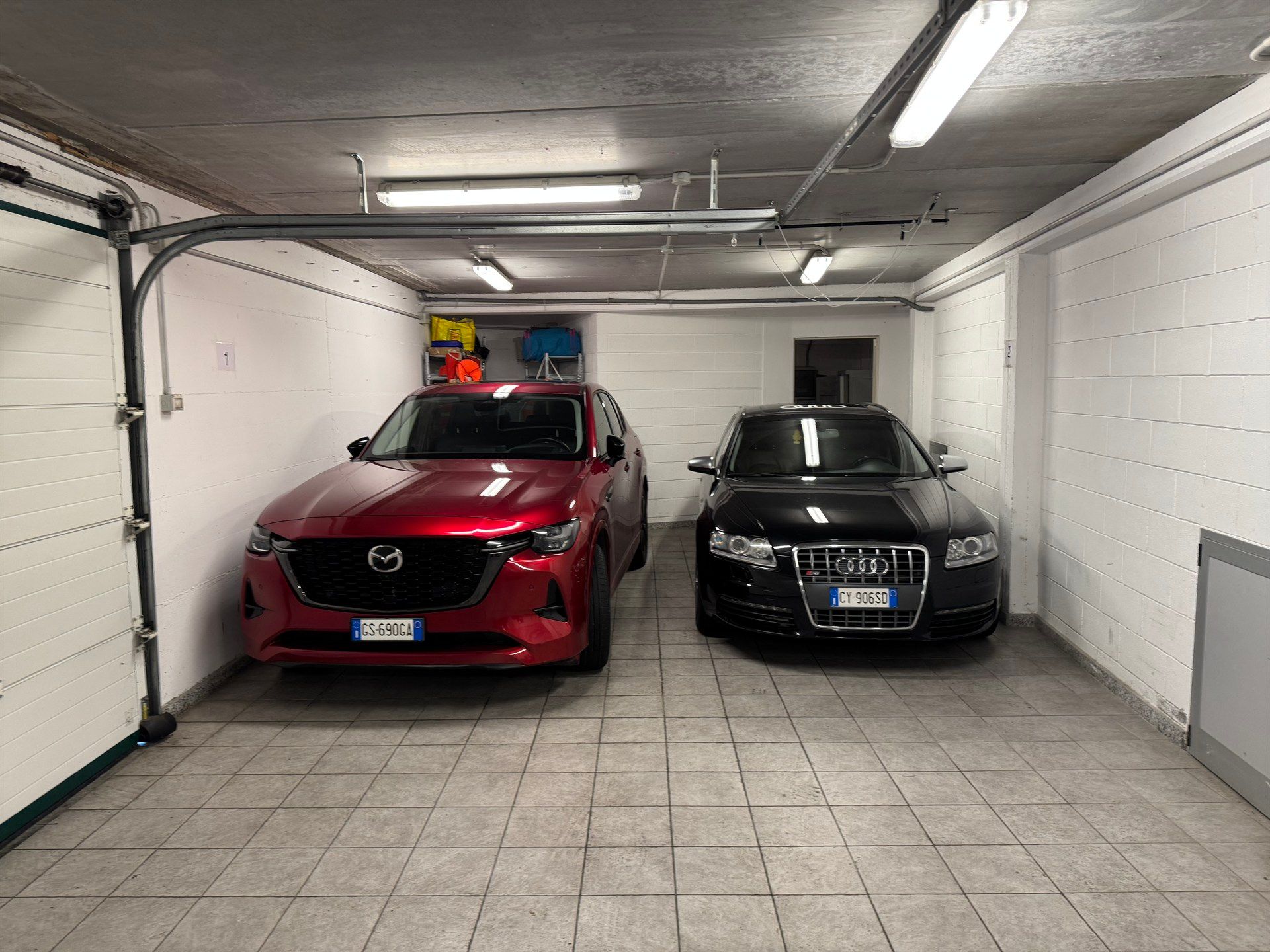 Two cars are parked in a garage next to each other.