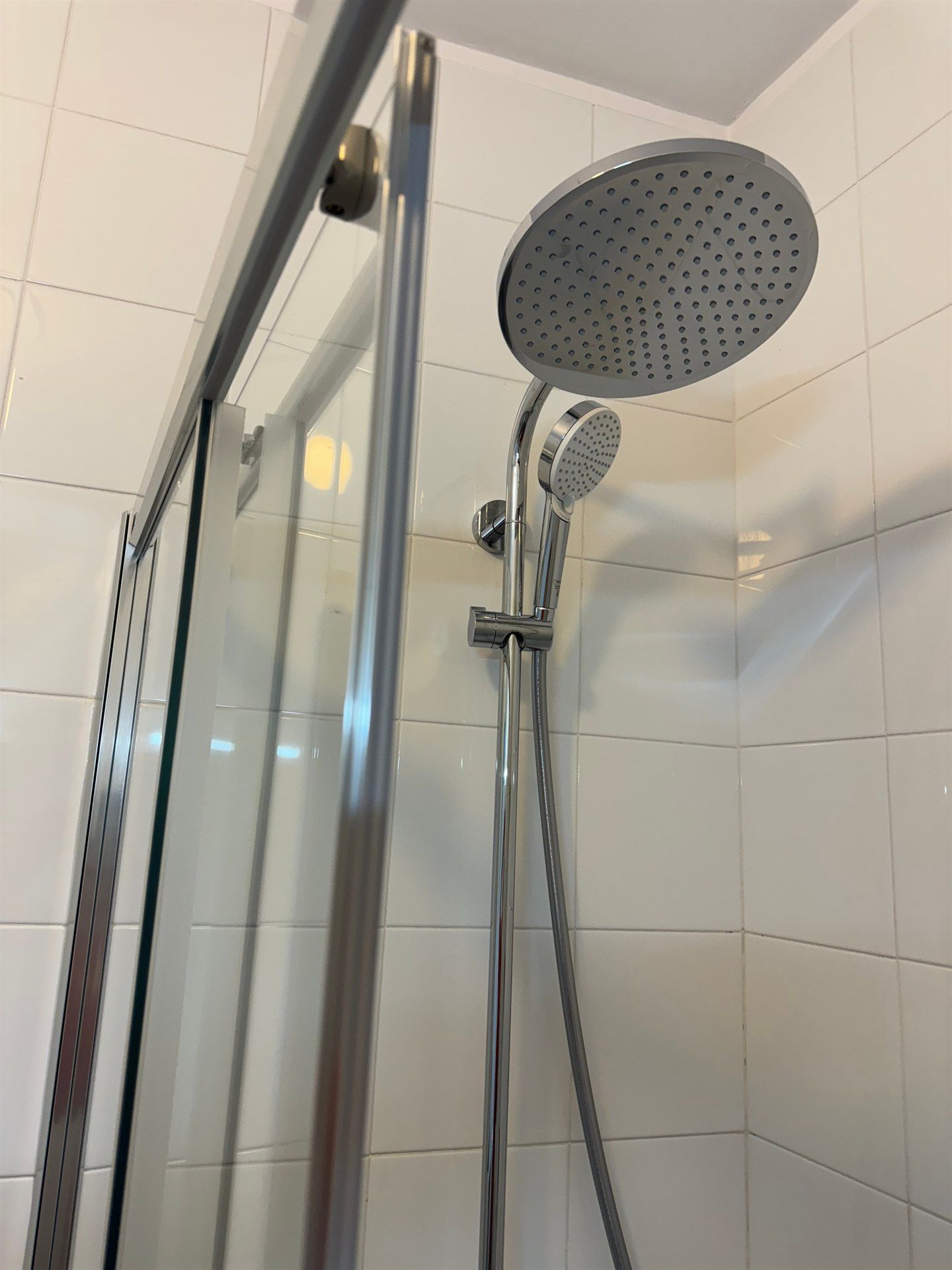 There is a shower head in the shower with a glass door.