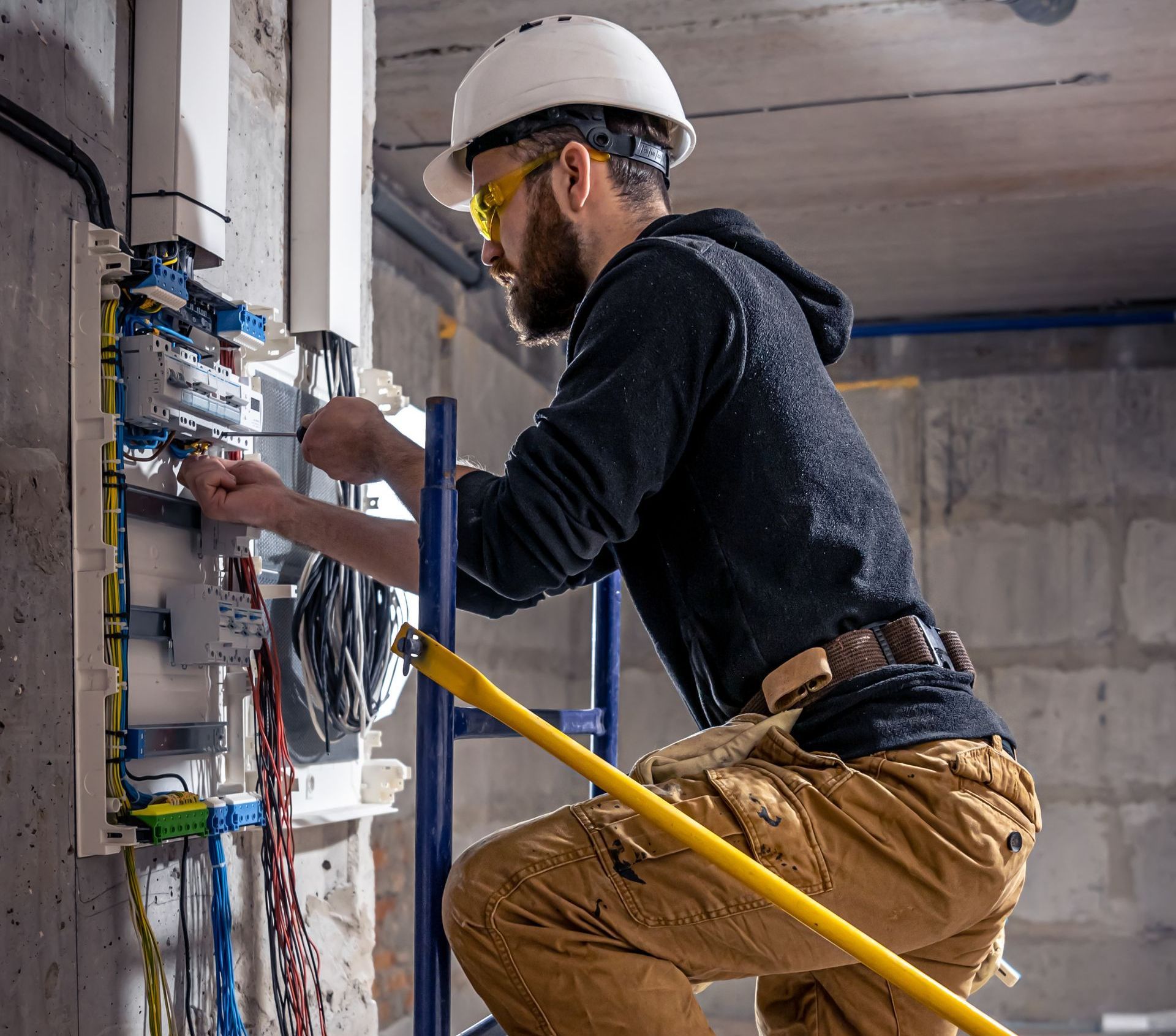 A man is kneeling on a ladder working on an electrical box.