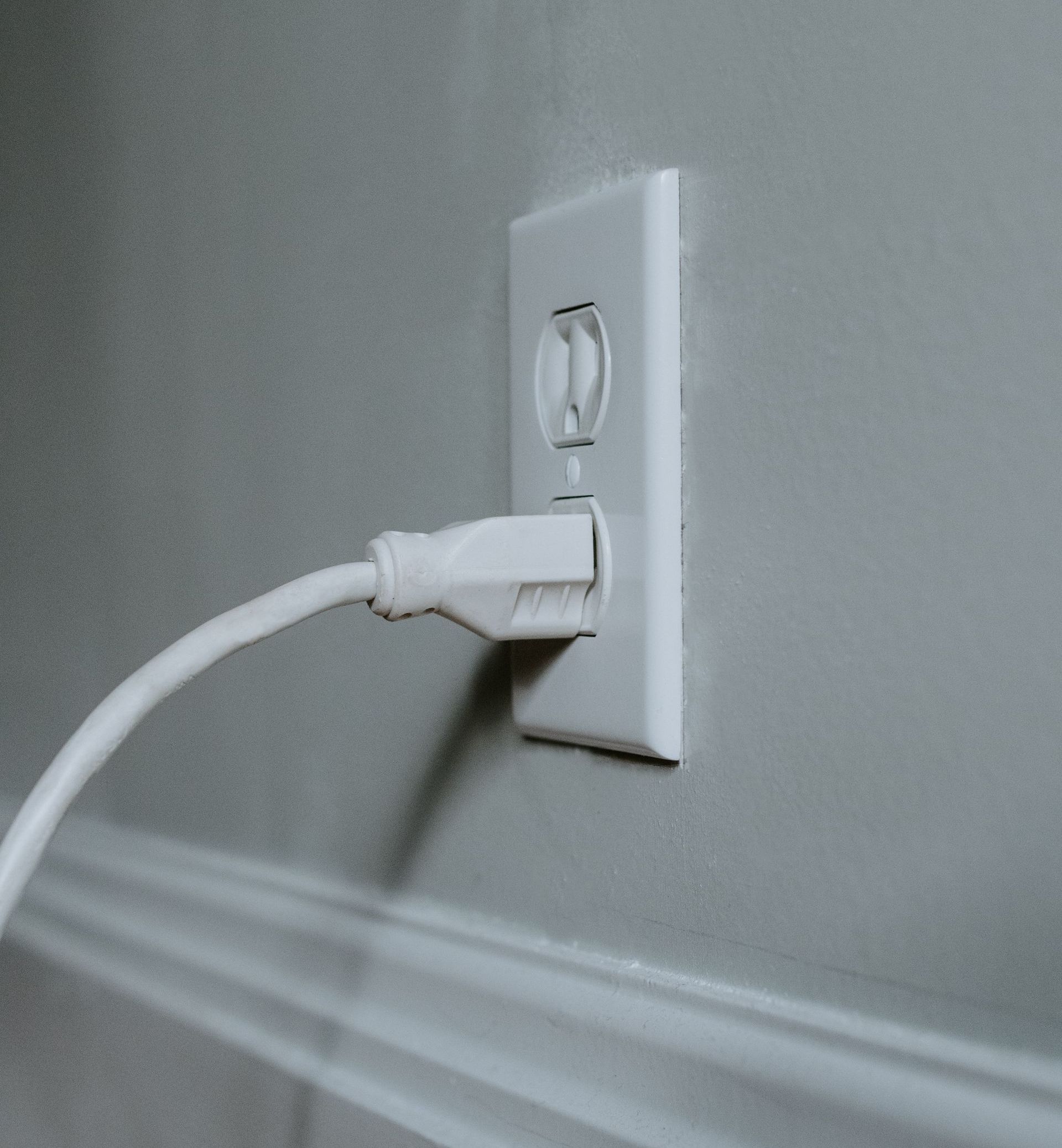 A white cord is plugged into a white wall outlet