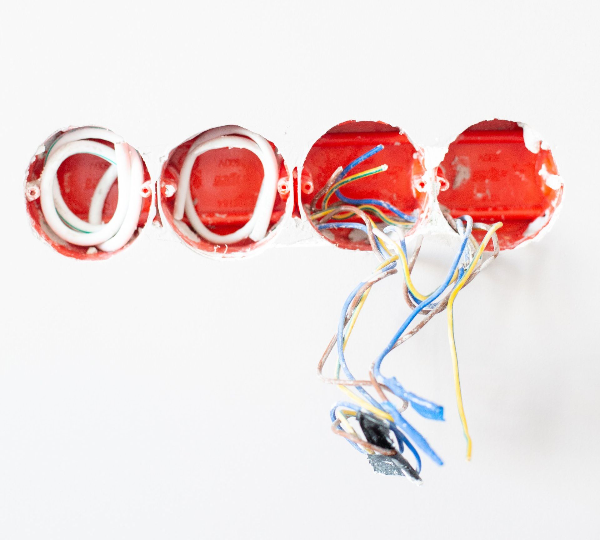 Three red electrical boxes with wires coming out of them on a white wall.