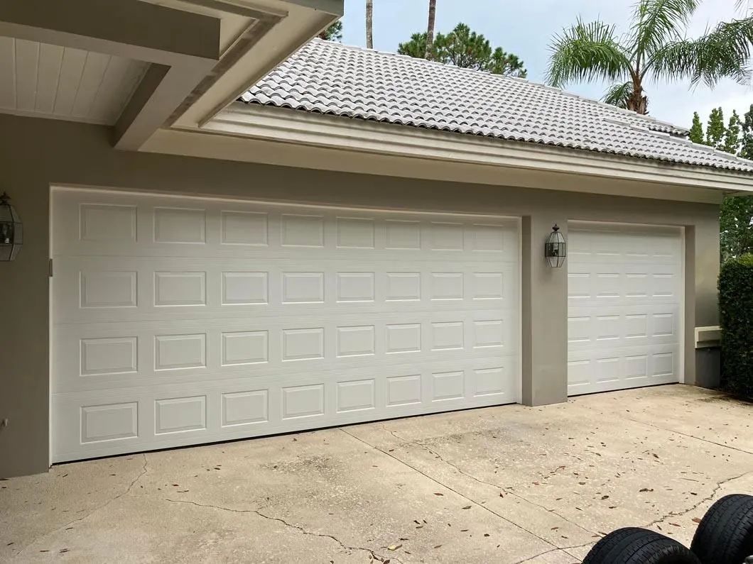 White two-car garage doors on a beige house with a sloped tiled roof and concrete driveway