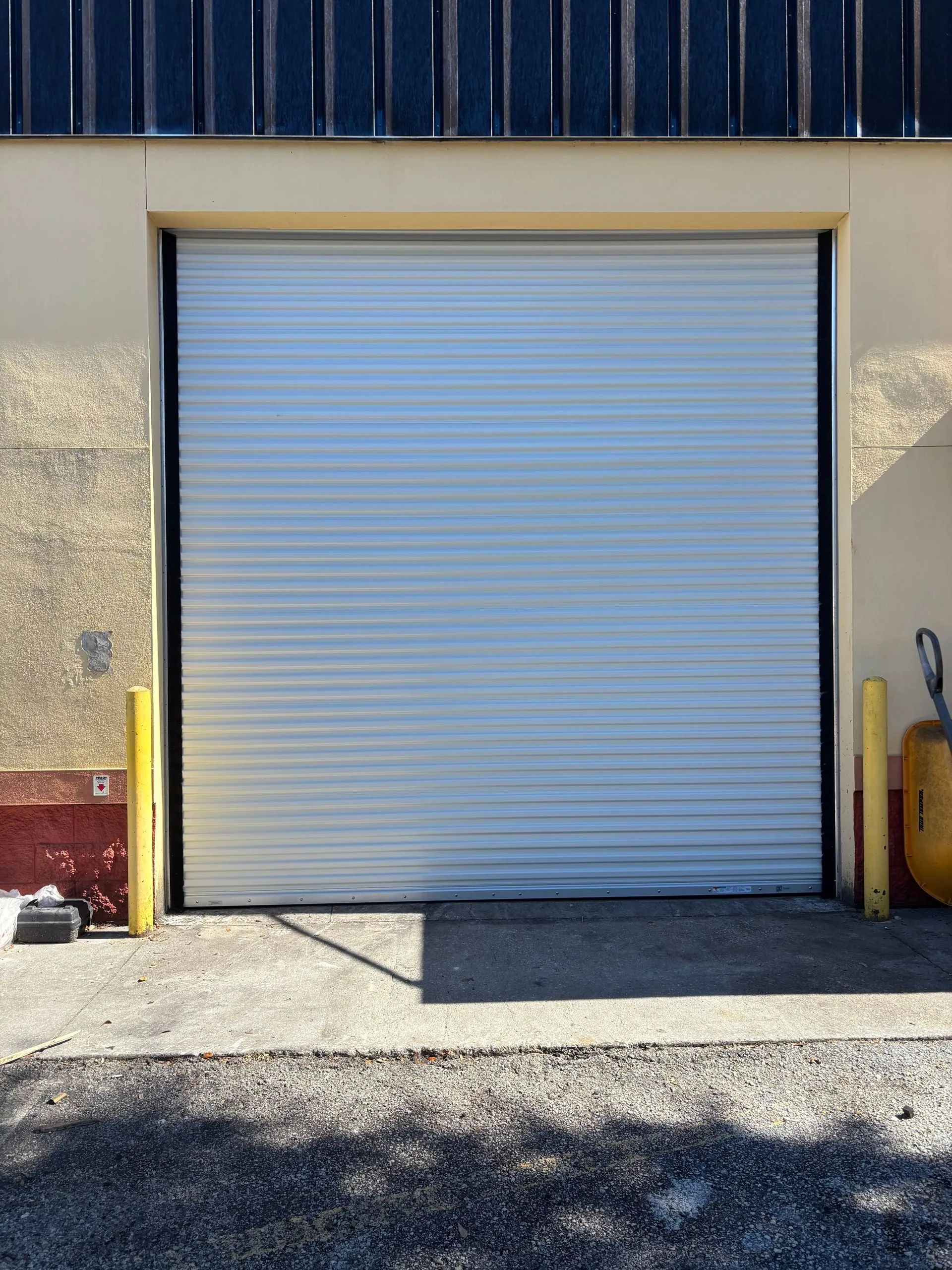 Closed white roll-up garage door on a warehouse building with yellow bollards at the sides