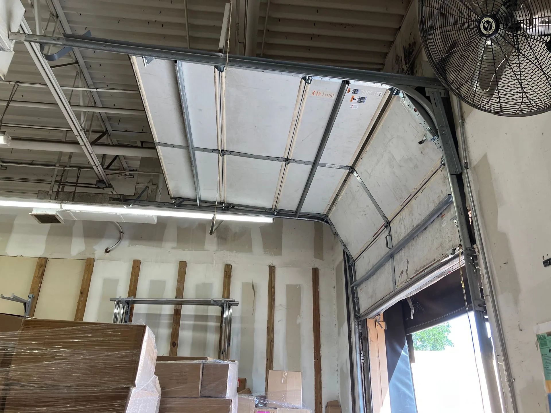 Warehouse interior with high metal ceiling, stacked pallets, and an open loading bay door with daylight.