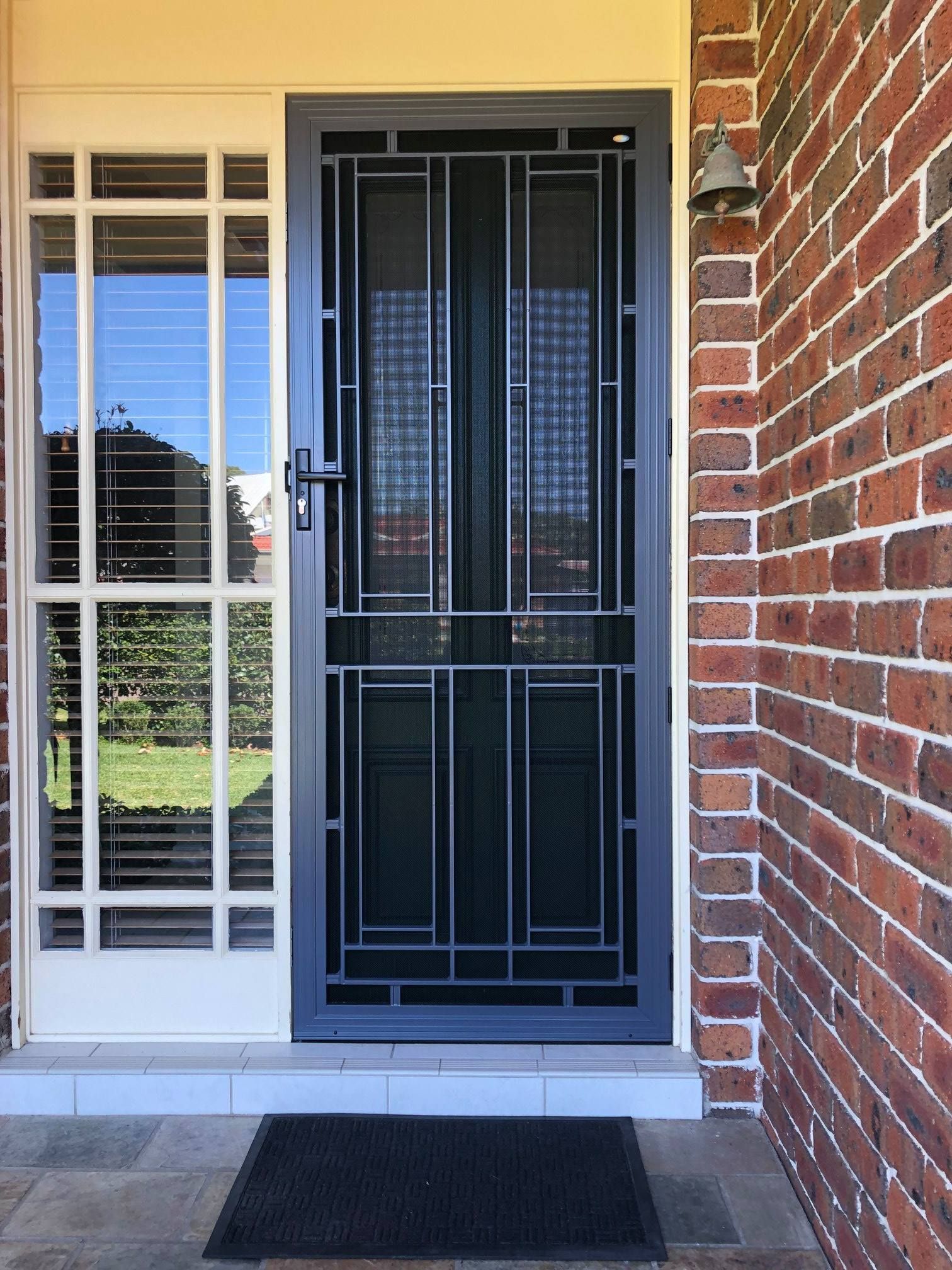 A black door with a screen on it is on a brick wall.