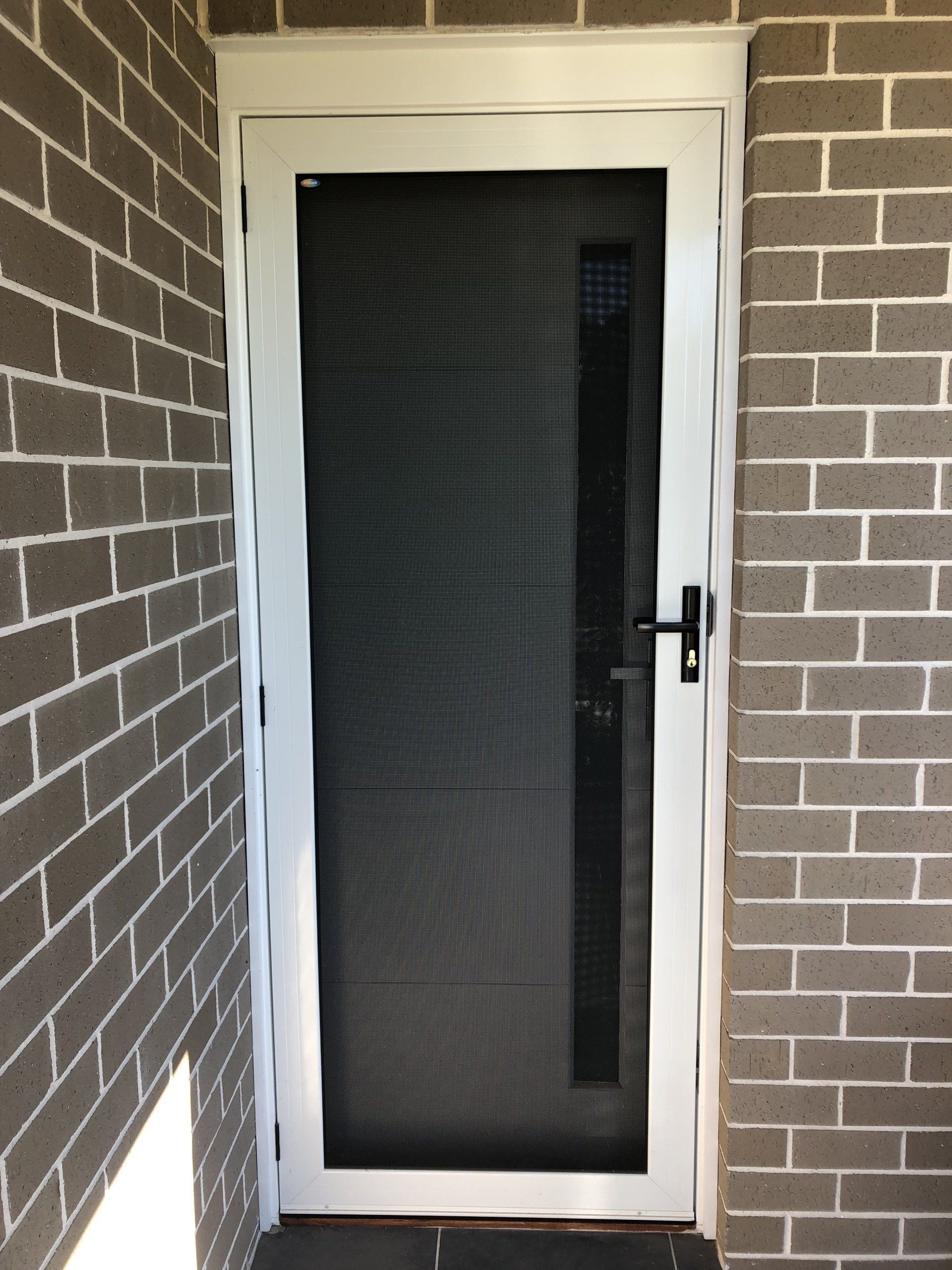 A white screen door is on a brick wall