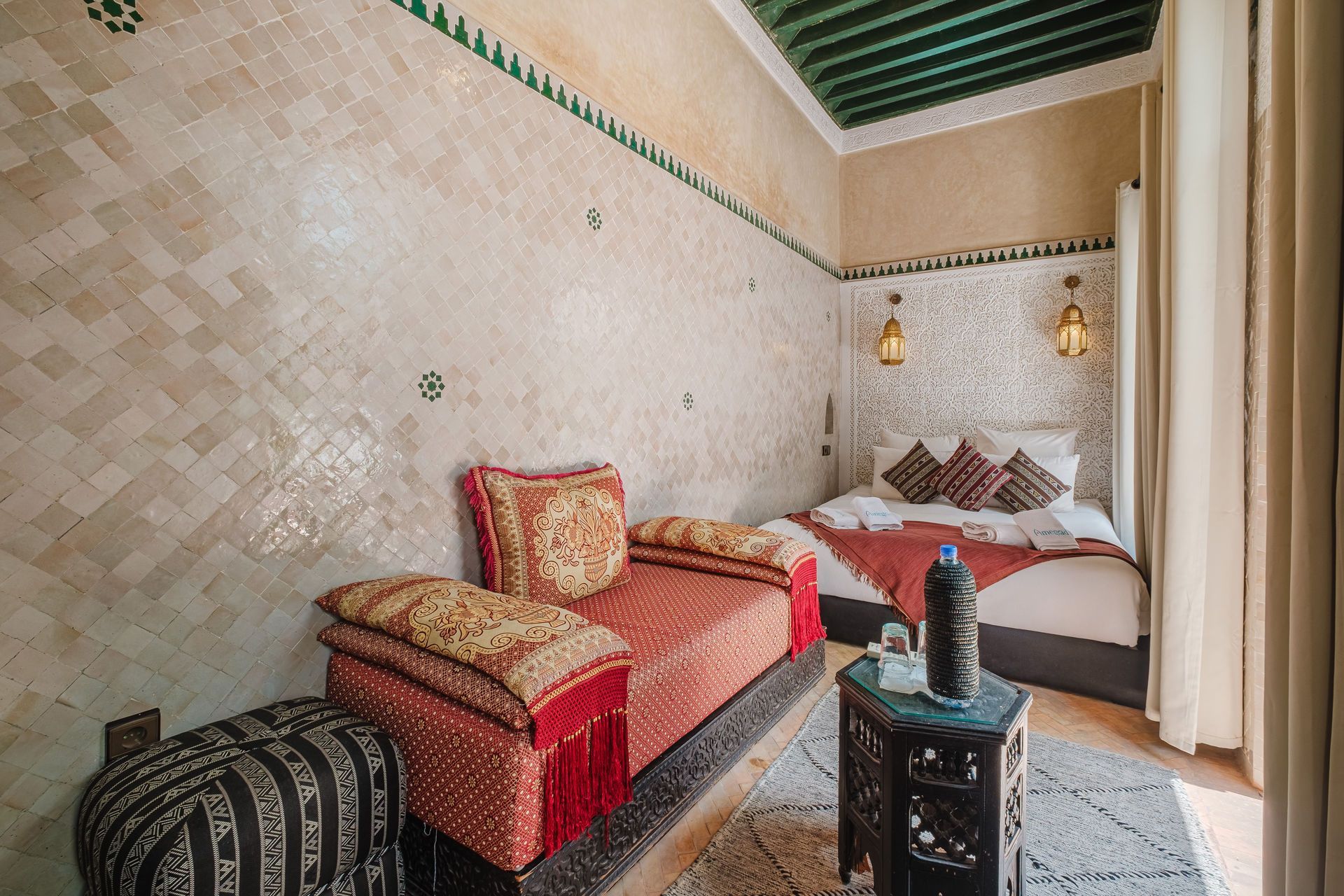 Cozy Moroccan bedroom: red seating, patterned tiles, lanterns, small table, bed with pillows.
