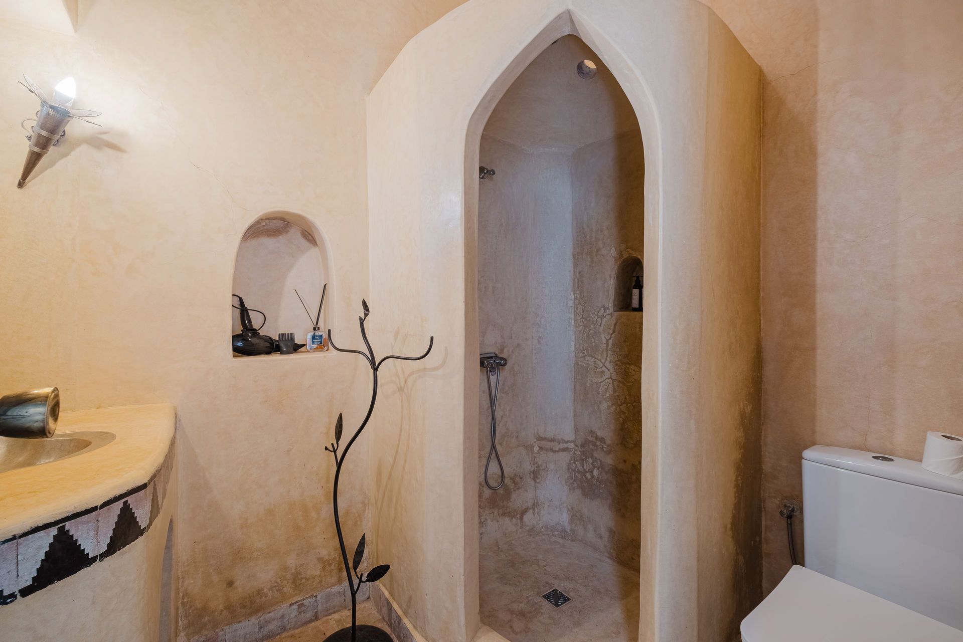Bathroom with arched shower, tan walls, toilet on right, black and white counter, and decorative metal fixture.