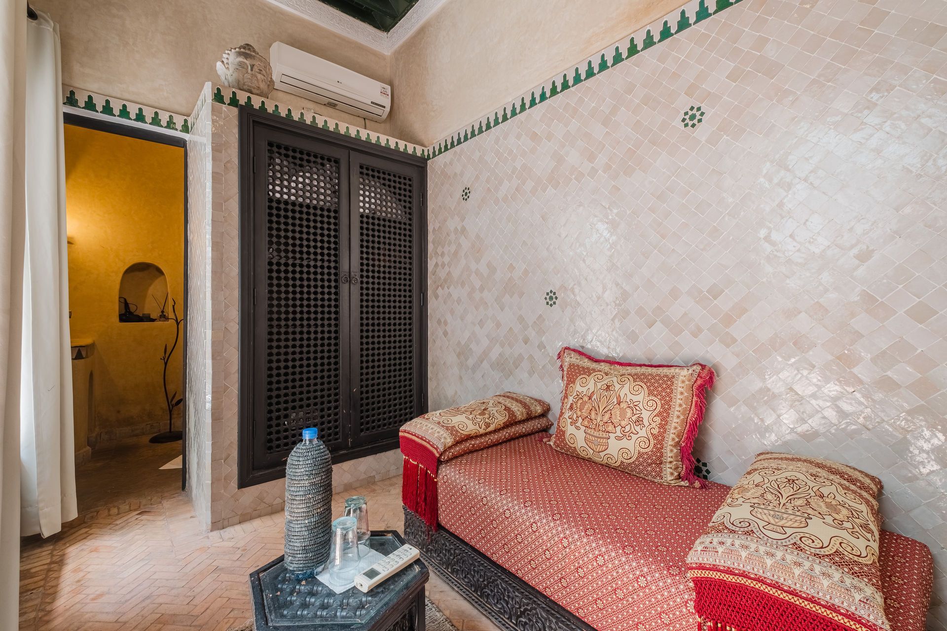 Bedroom with a red sofa, decorative mosaic wall, dark wood cabinet, and a doorway leading to a bathroom.