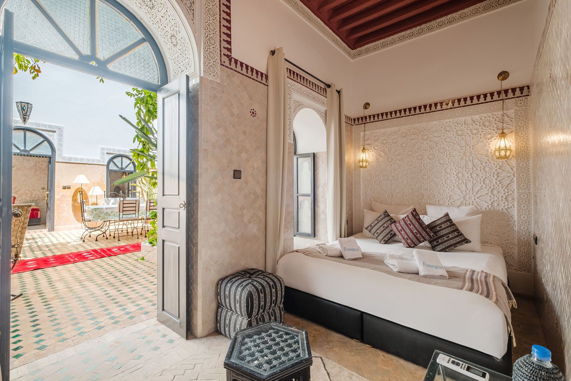 Bedroom in Moroccan riad with open doorway to patio; white walls, ornate details, king bed.