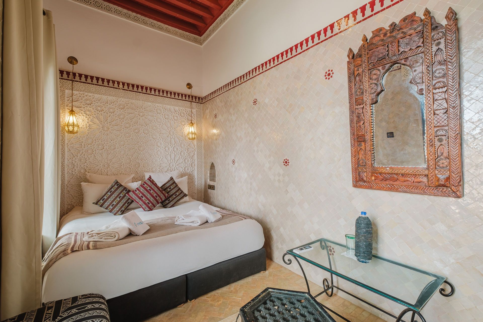 Cozy bedroom with bed, decorative mirror, glass table, and patterned walls and ceiling.