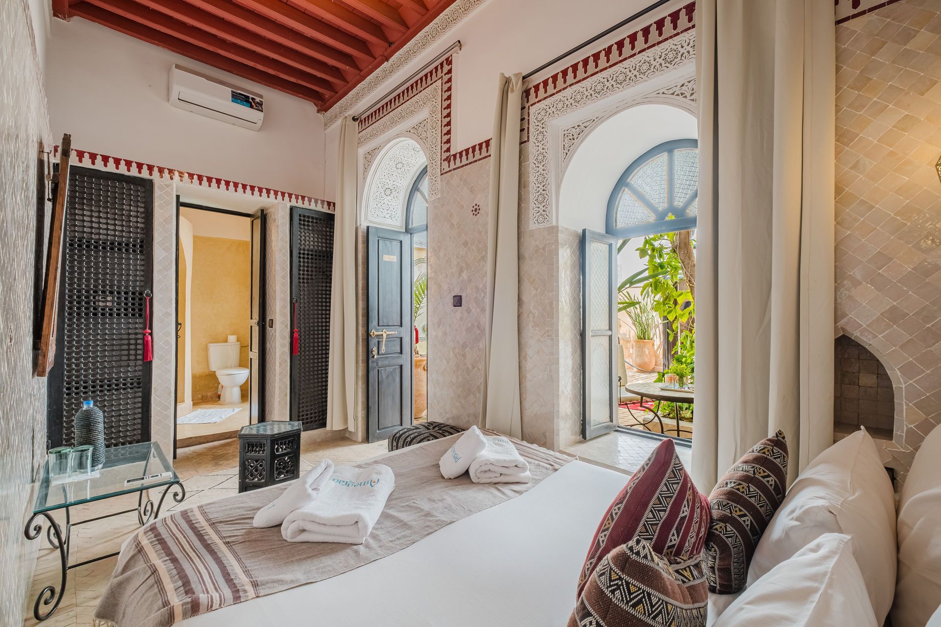 Bedroom with arched doorways, bed, and view to a courtyard. Red accents, white walls.