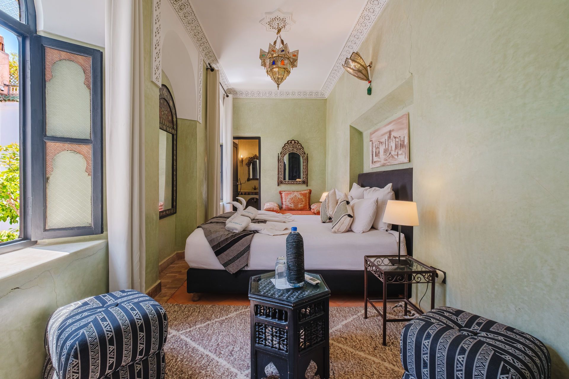 Bedroom with green walls, ornate archways, a bed, and patterned poufs.