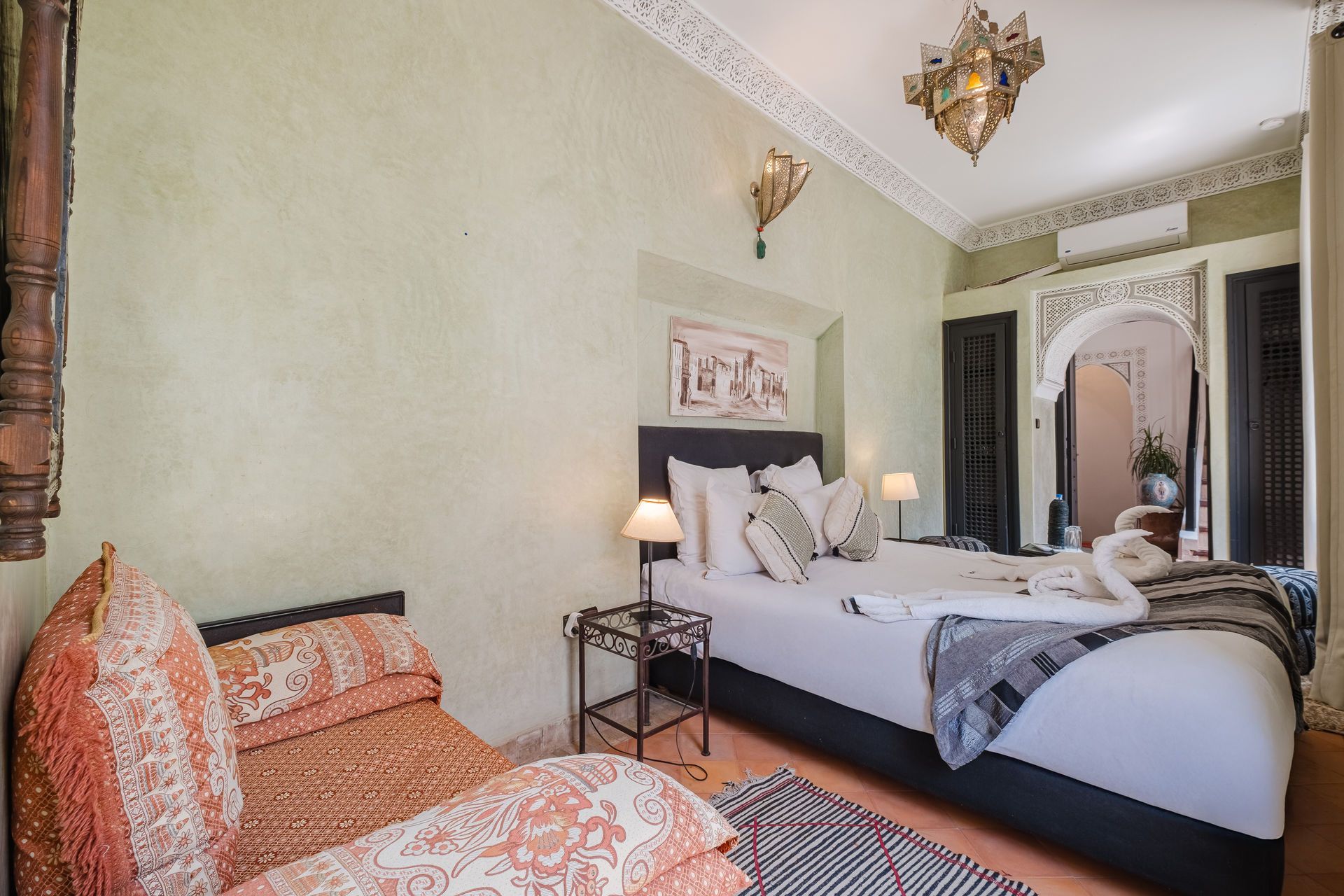 Bedroom with bed, couch, ornate doorway, and decorative ceiling lights.