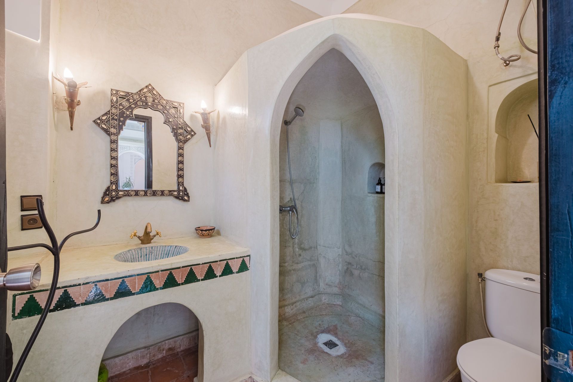 Moroccan-style bathroom with arched shower and sink, decorated with detailed tilework and mirror.