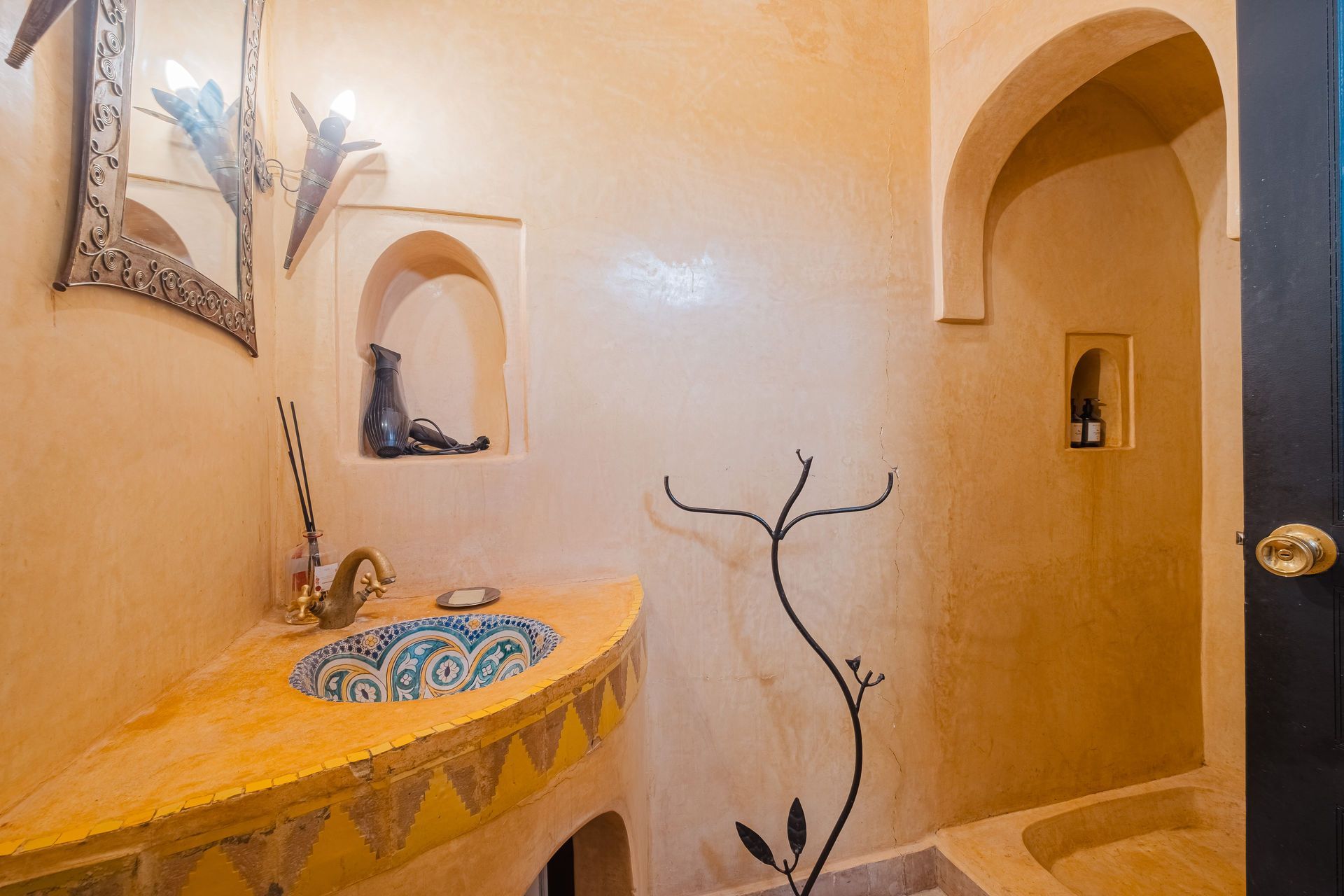 Moroccan-style bathroom with arched doorway, curved sink with blue design, and tan walls.