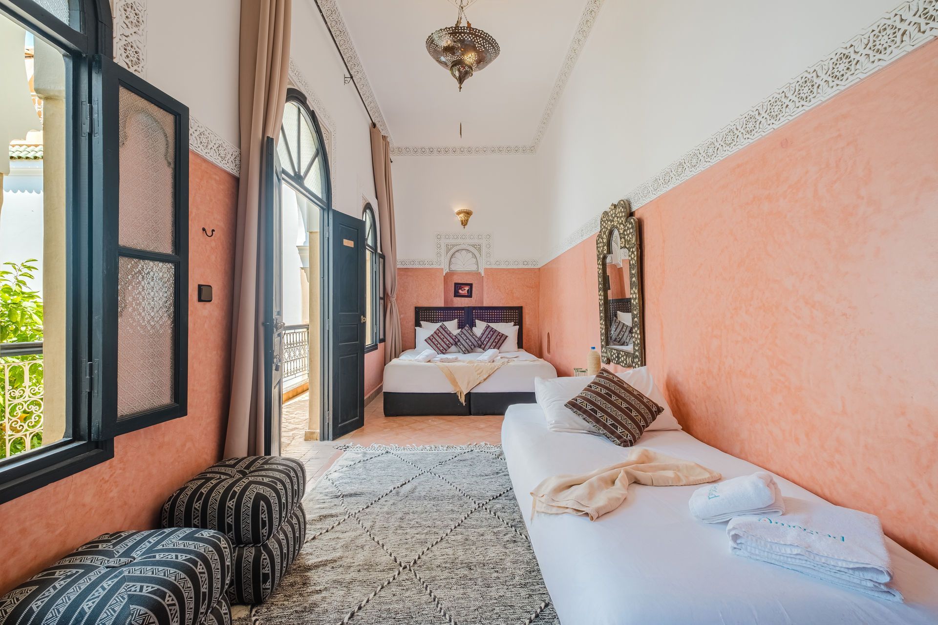 Bedroom with peach walls, two beds, a balcony, and traditional Moroccan decor.