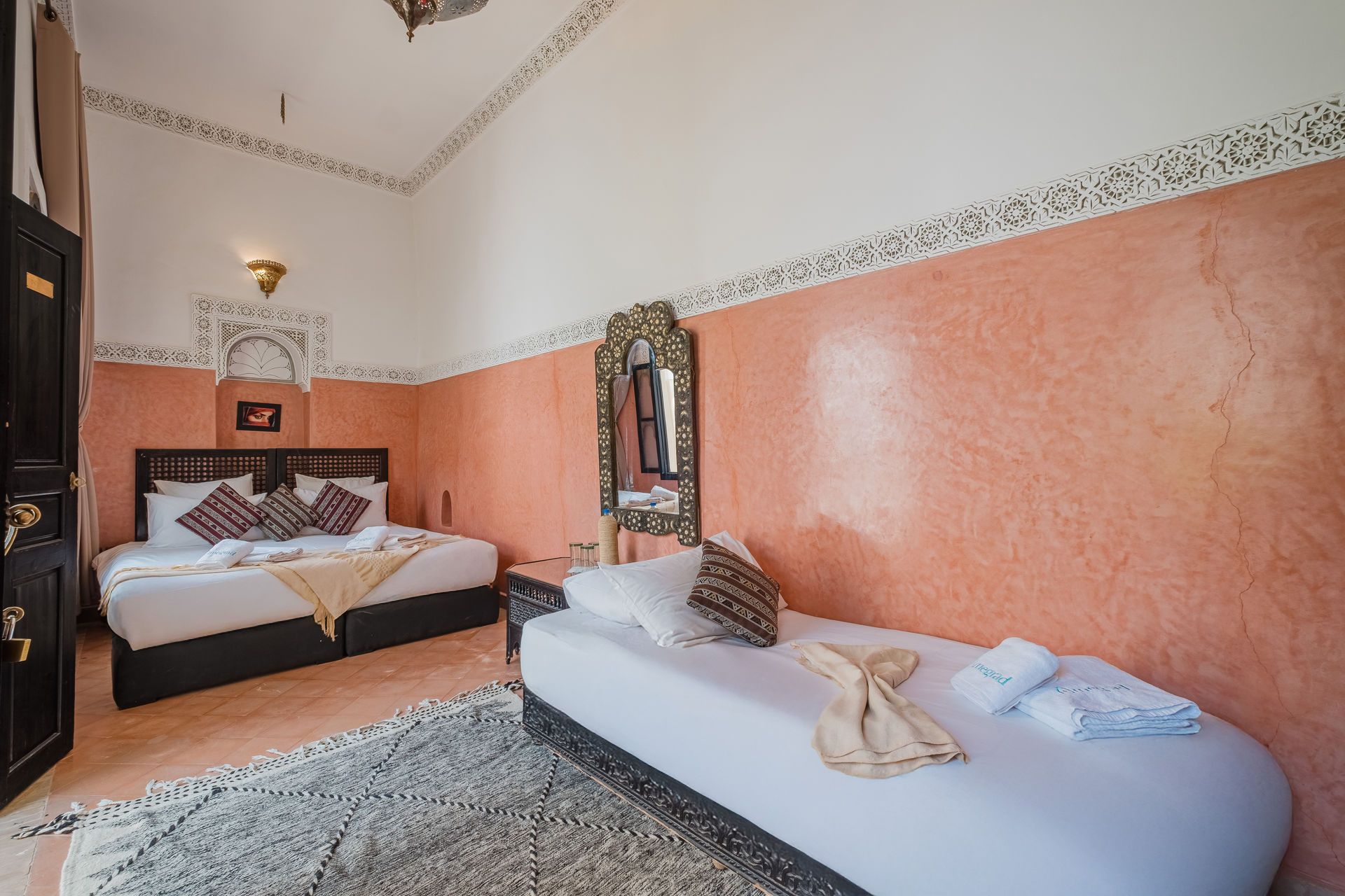 Bedroom with two beds, peach walls, ornate trim, rug, and mirror.