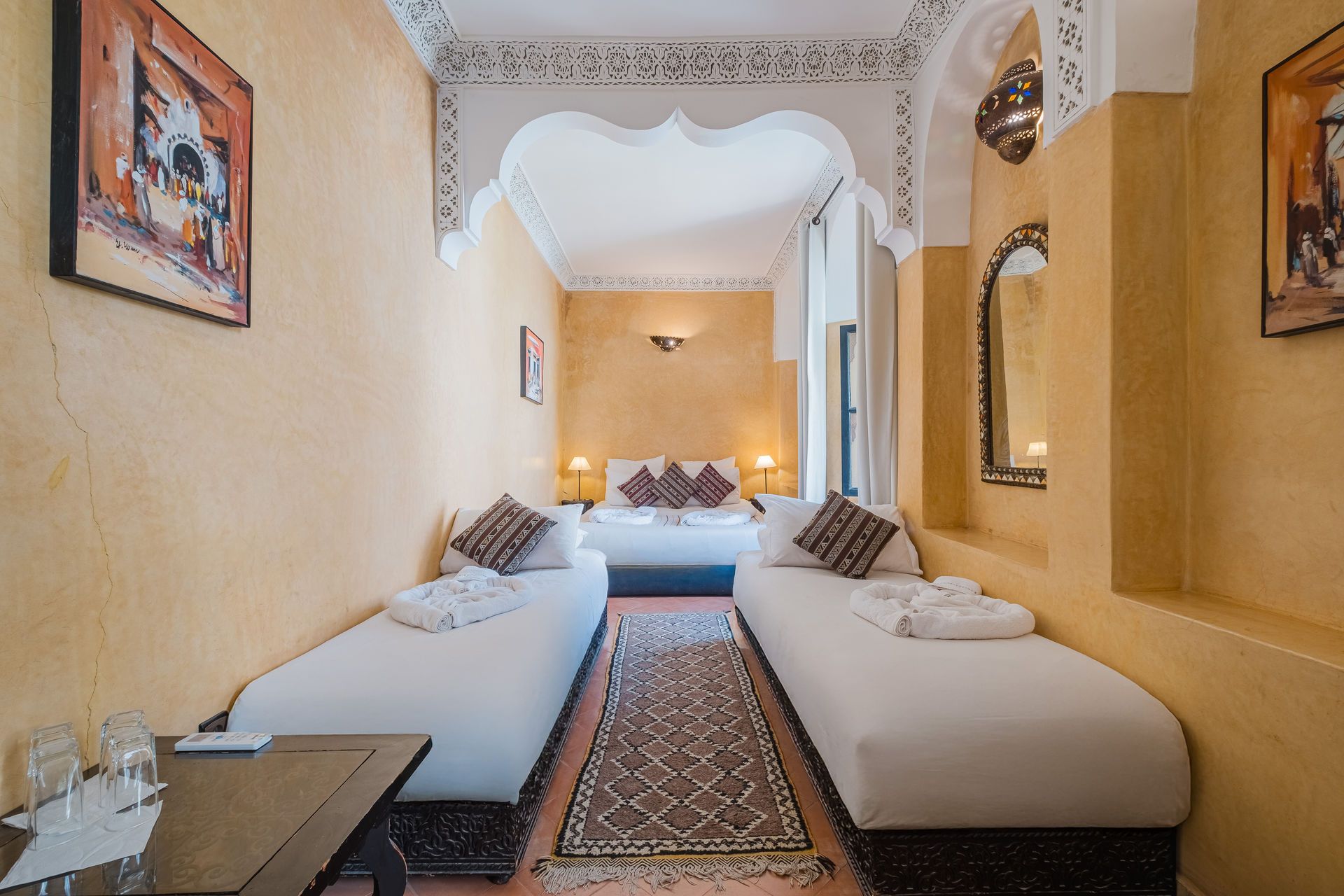 Moroccan-style bedroom with three beds, ornate archway, and yellow walls.