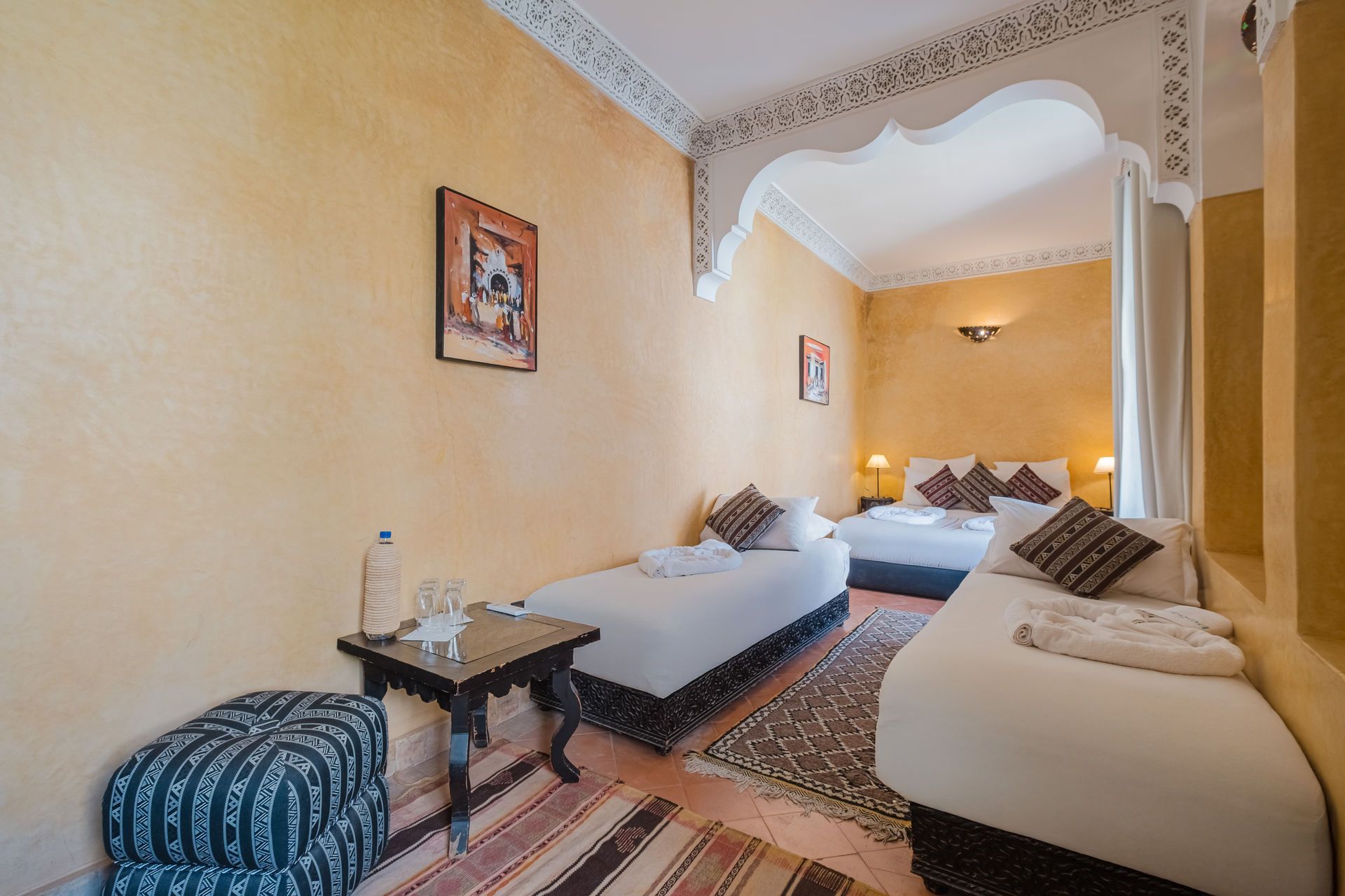 Bedroom in a Moroccan riad with three beds, a small table, and patterned rug.