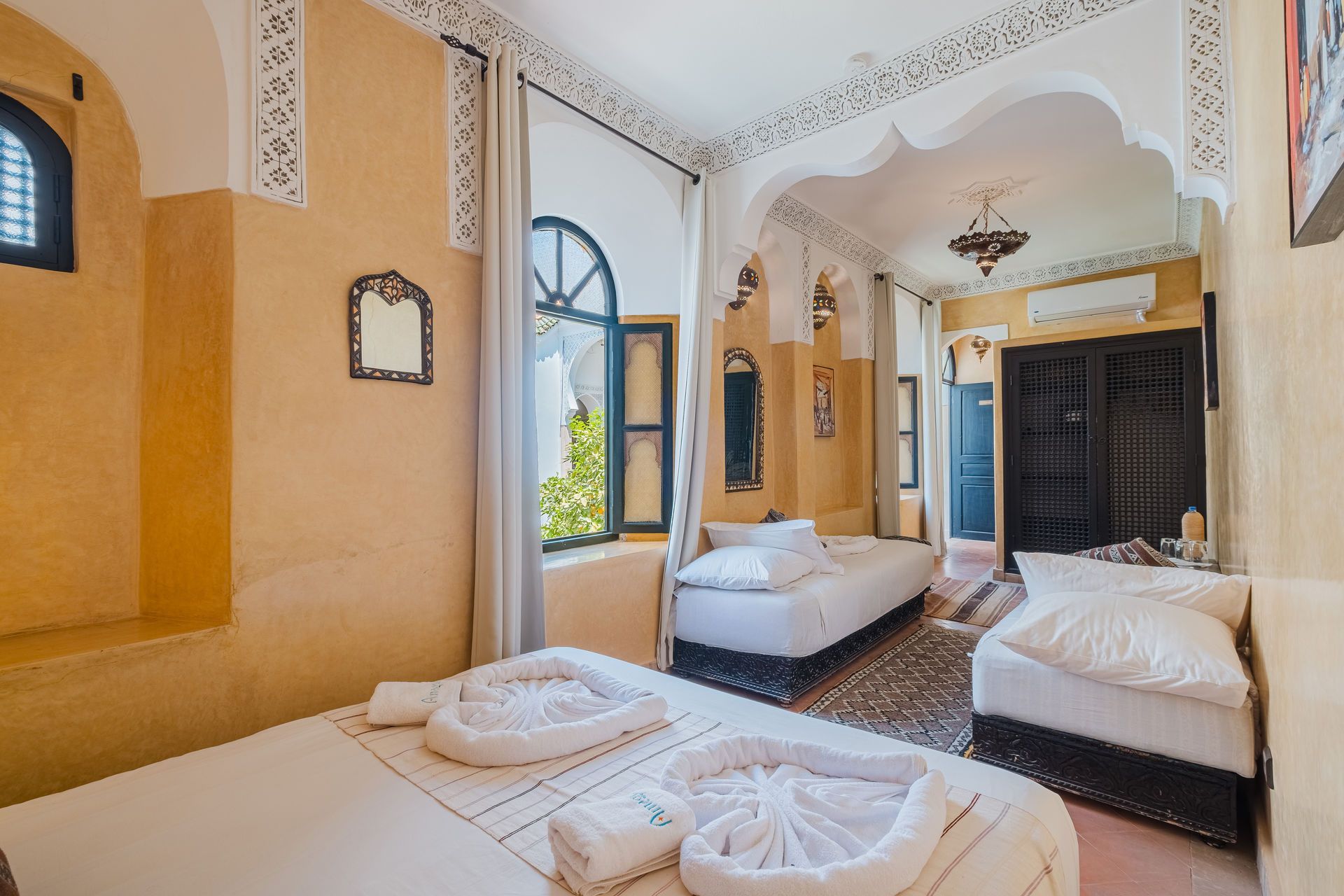 A room with three beds, a window, and ornate white trim. Walls are yellow, and a dark closet is visible.