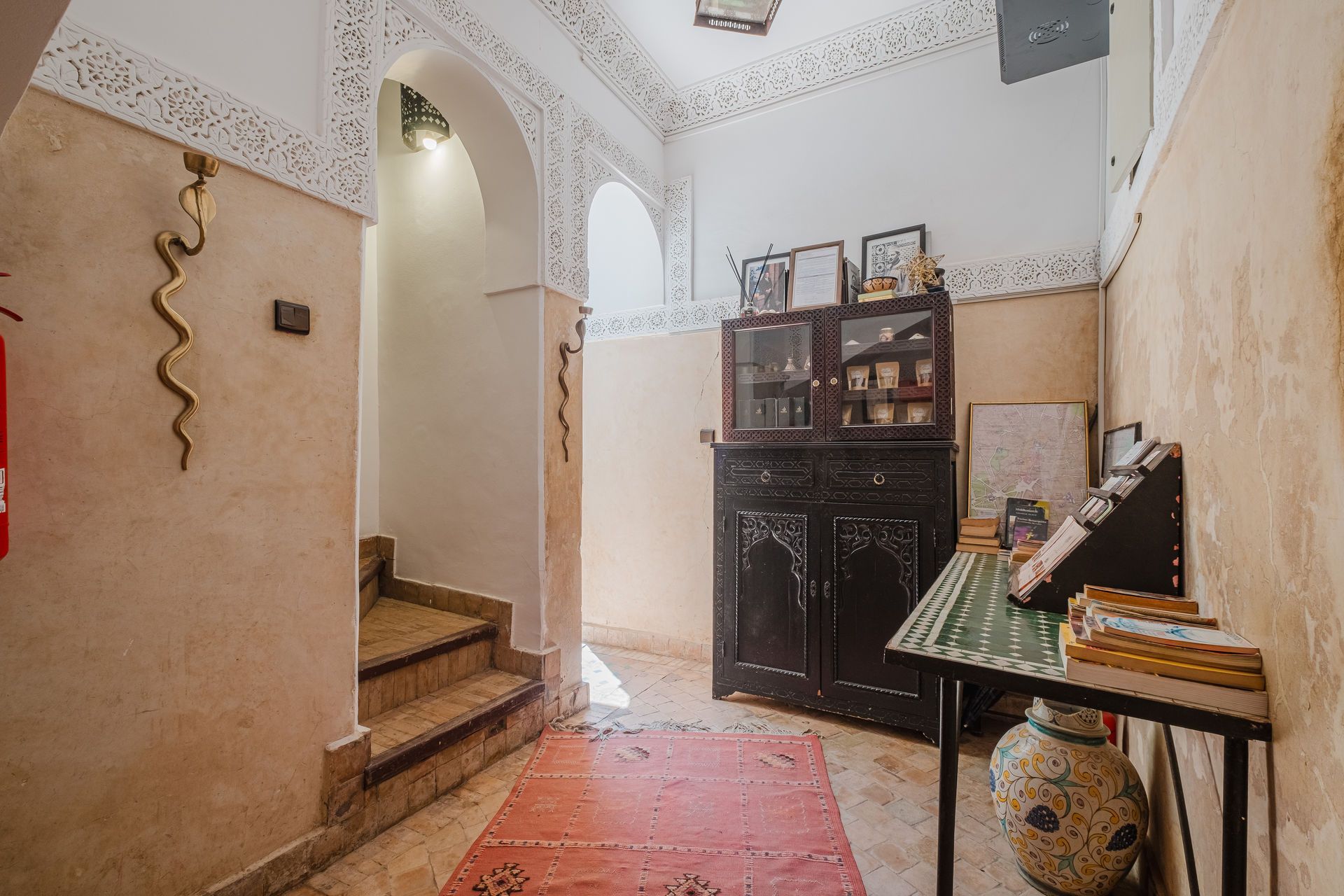 Hallway with stairs, ornate arches, dark cabinet, and decorative table; earthy tones.