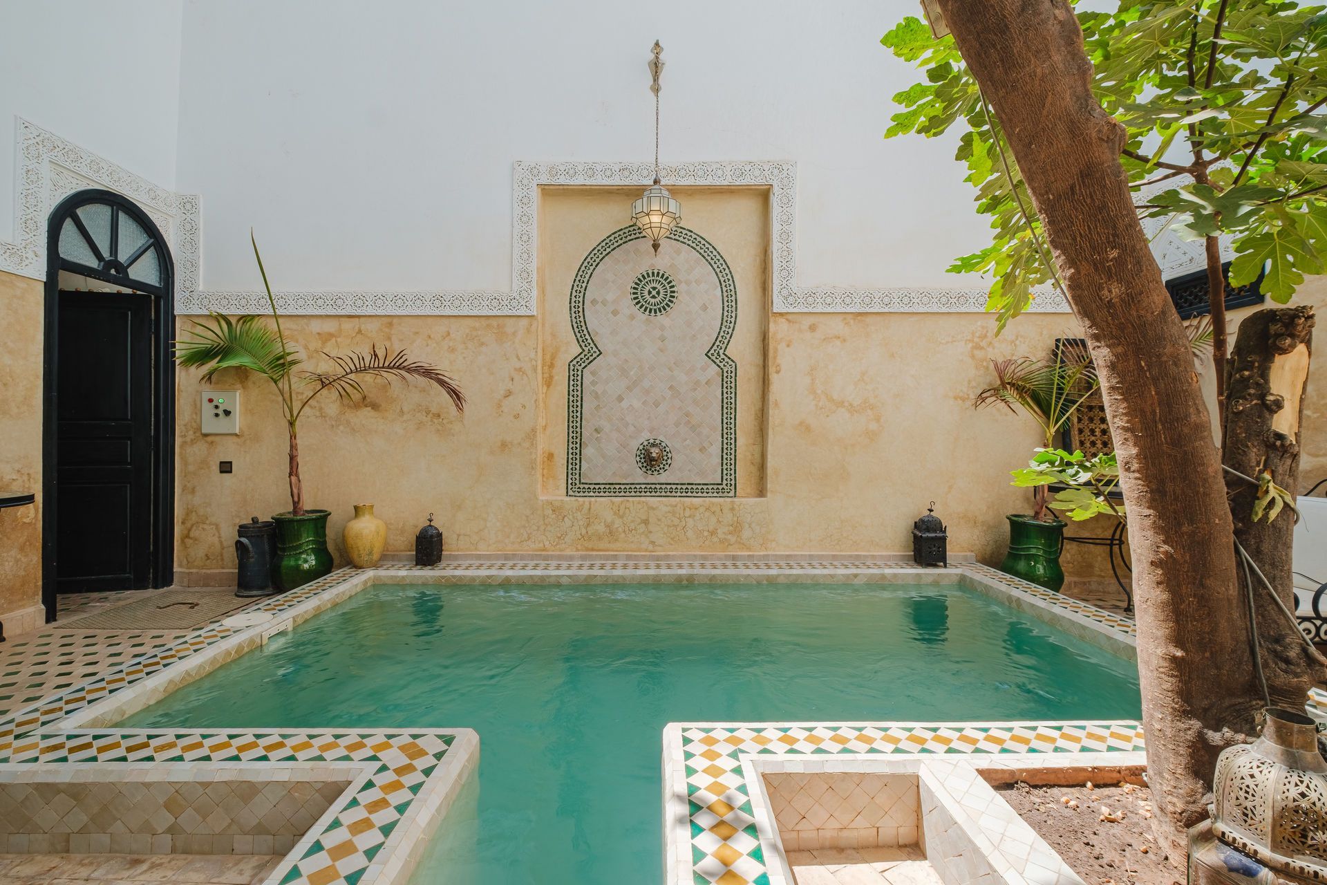 A courtyard with a small pool, decorated with tile, a central fountain, and an arched doorway.