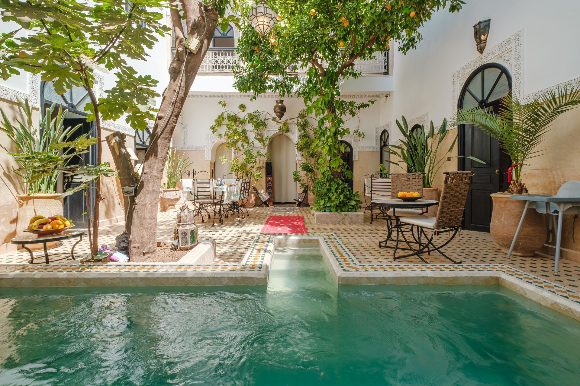 Courtyard with pool, seating areas, and a tree in a traditional Moroccan riad setting.