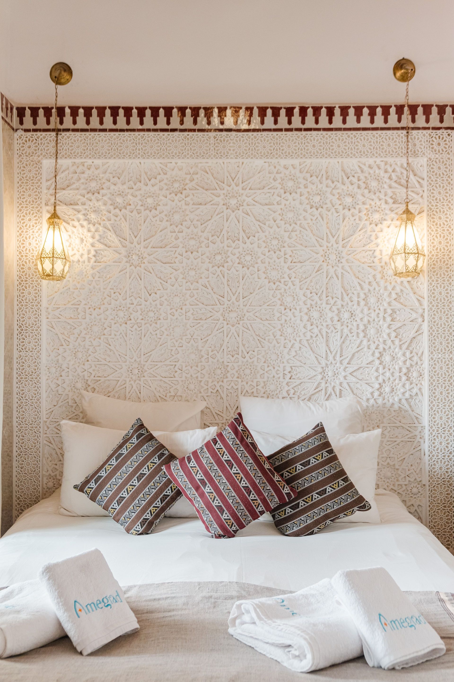 Bedroom with white bed, patterned pillows, ornate headboard, and hanging lanterns.