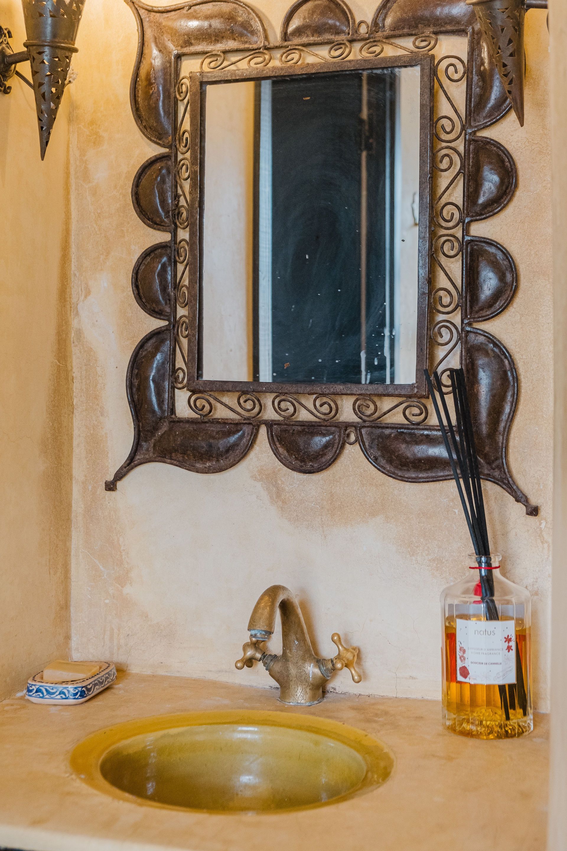 Bathroom sink with ornate bronze mirror, faucet, and decorative accents.