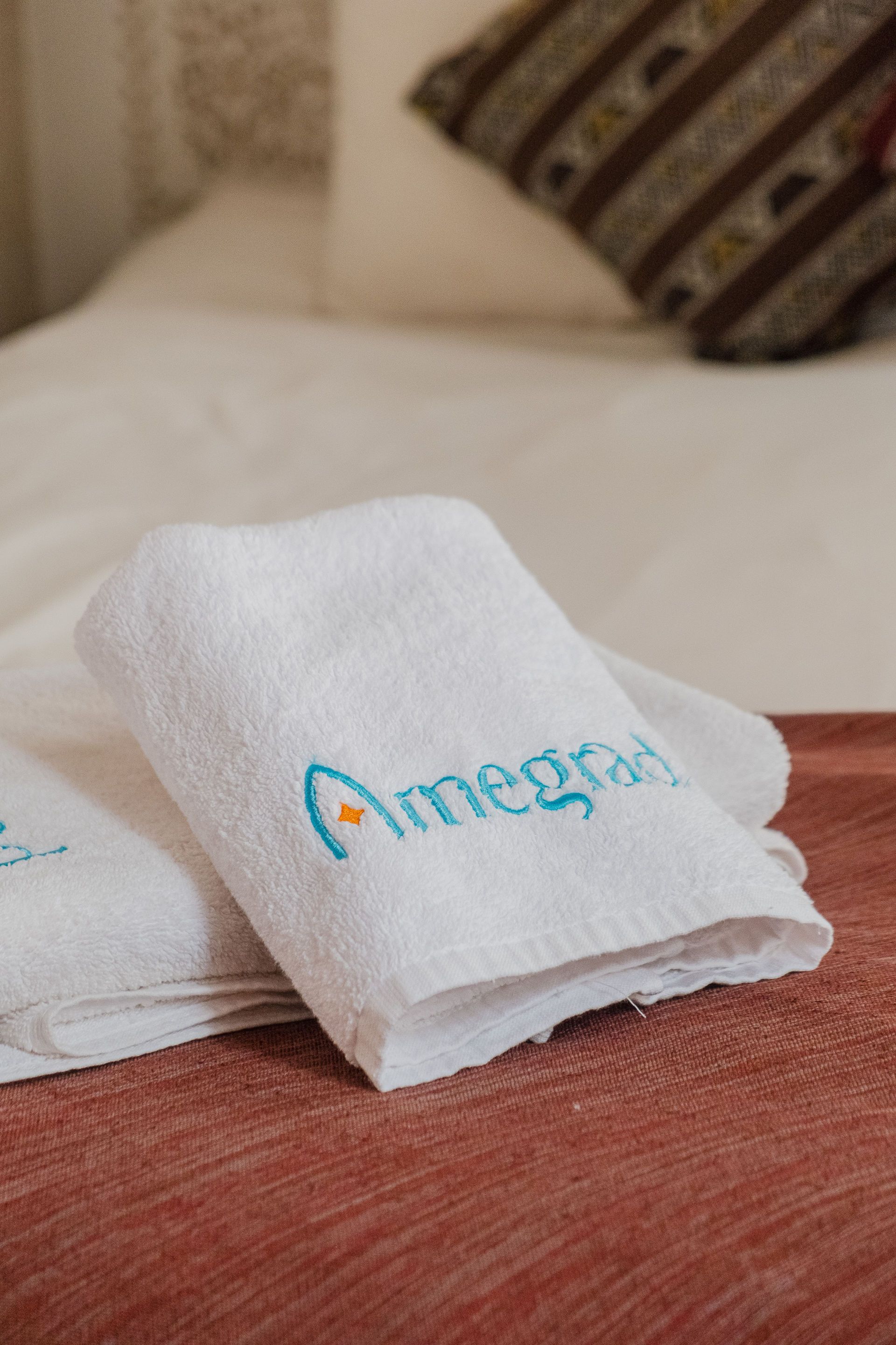White folded towels on a bed with teal logo 
