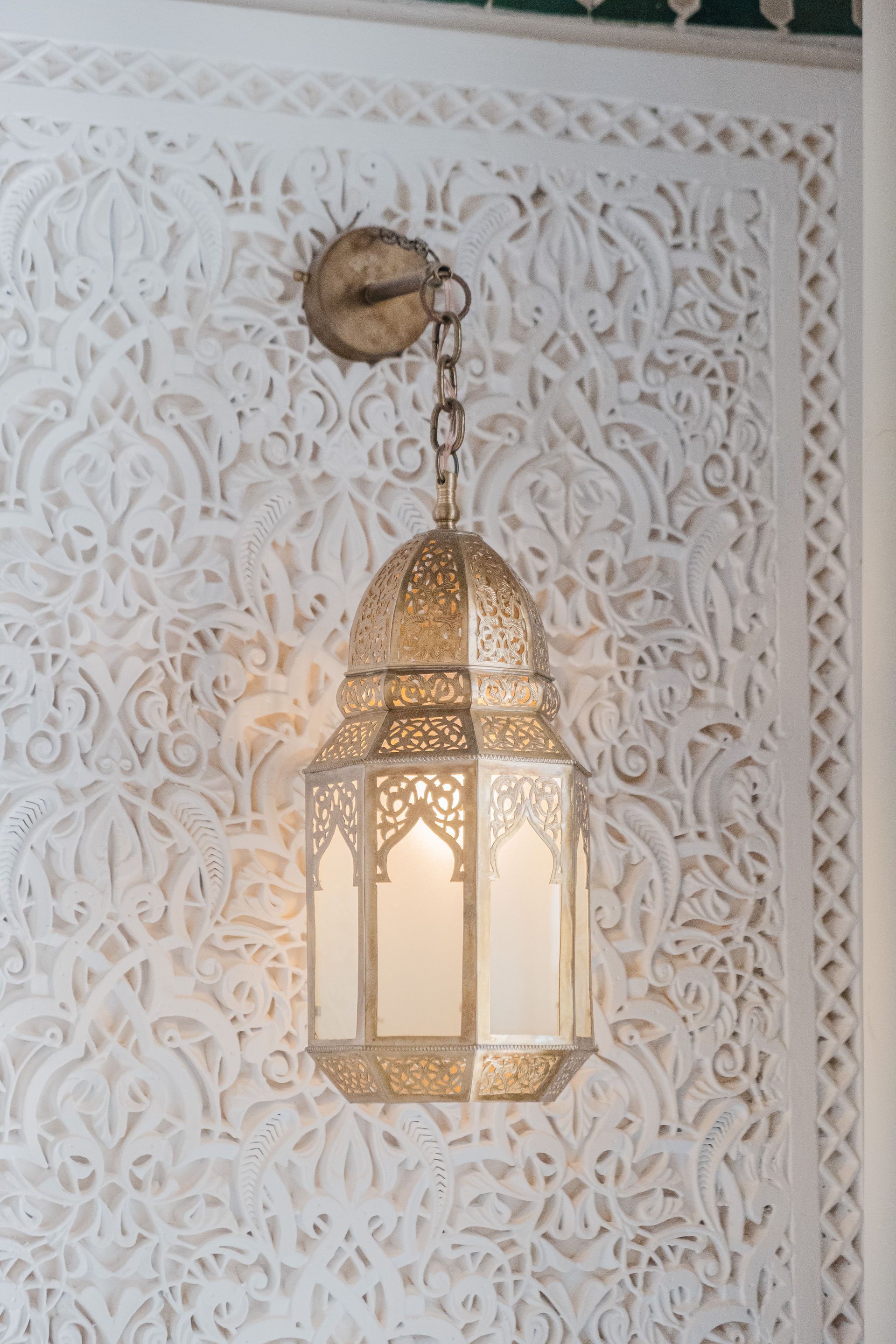 Ornate gold lantern hanging on a white carved wall, casting a warm light.
